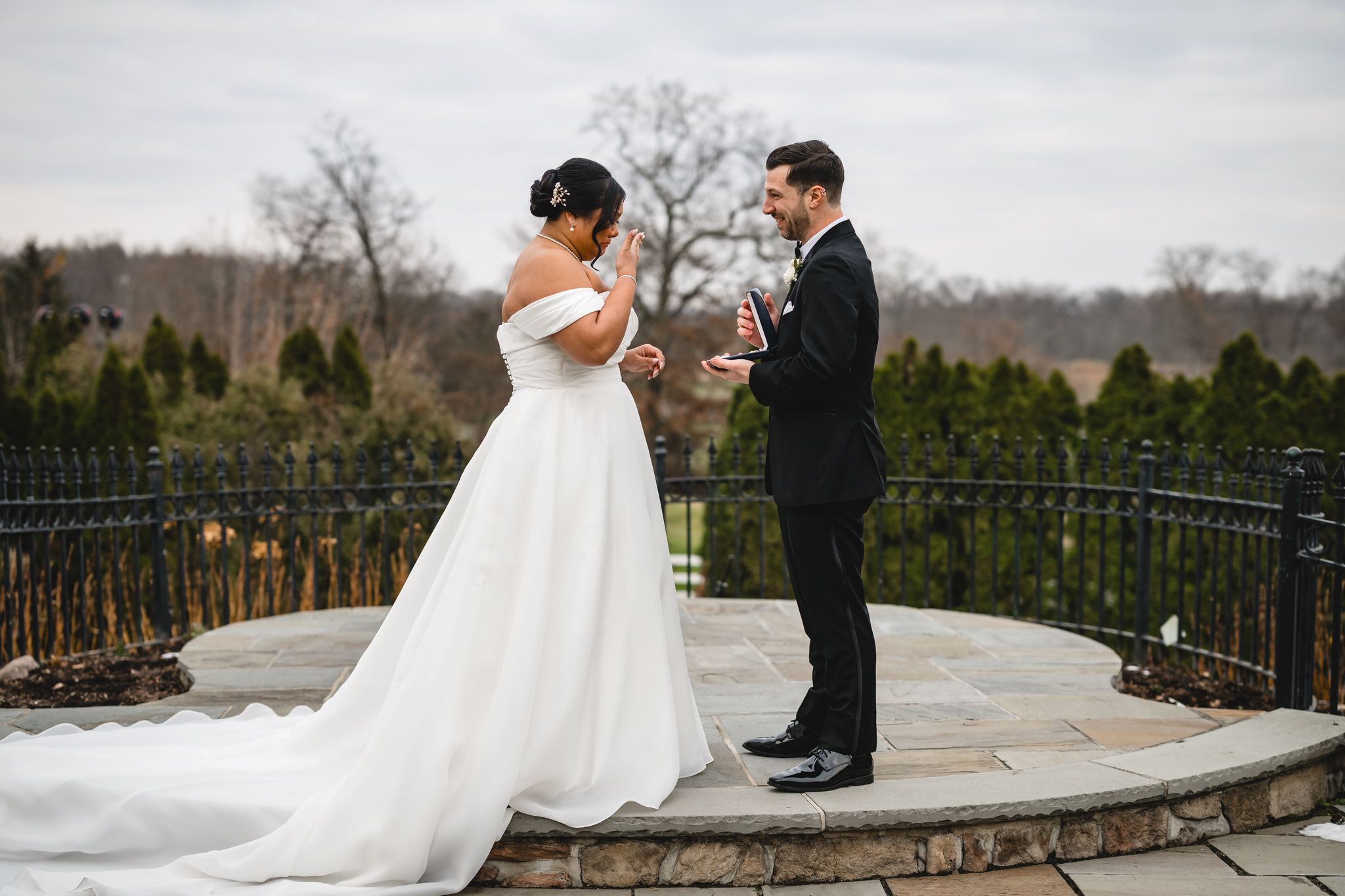 A couple shares an emotional first look moment on a stone terrace with winter landscape behind them.