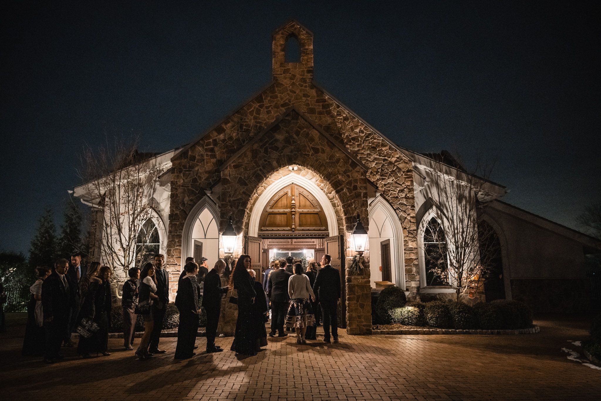 Panoramic nighttime view of illuminated chapel exterior during wedding ceremony.