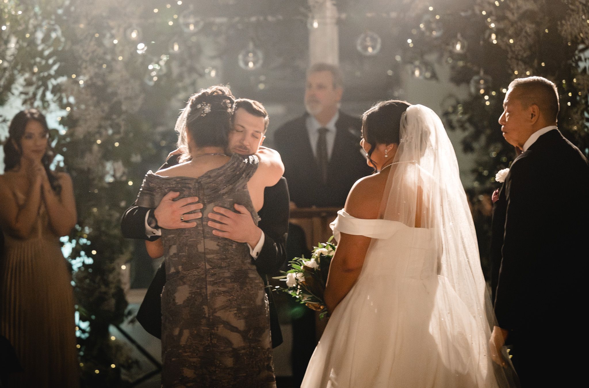Emotional moment during outdoor wedding ceremony with sunlight streaming through trees.