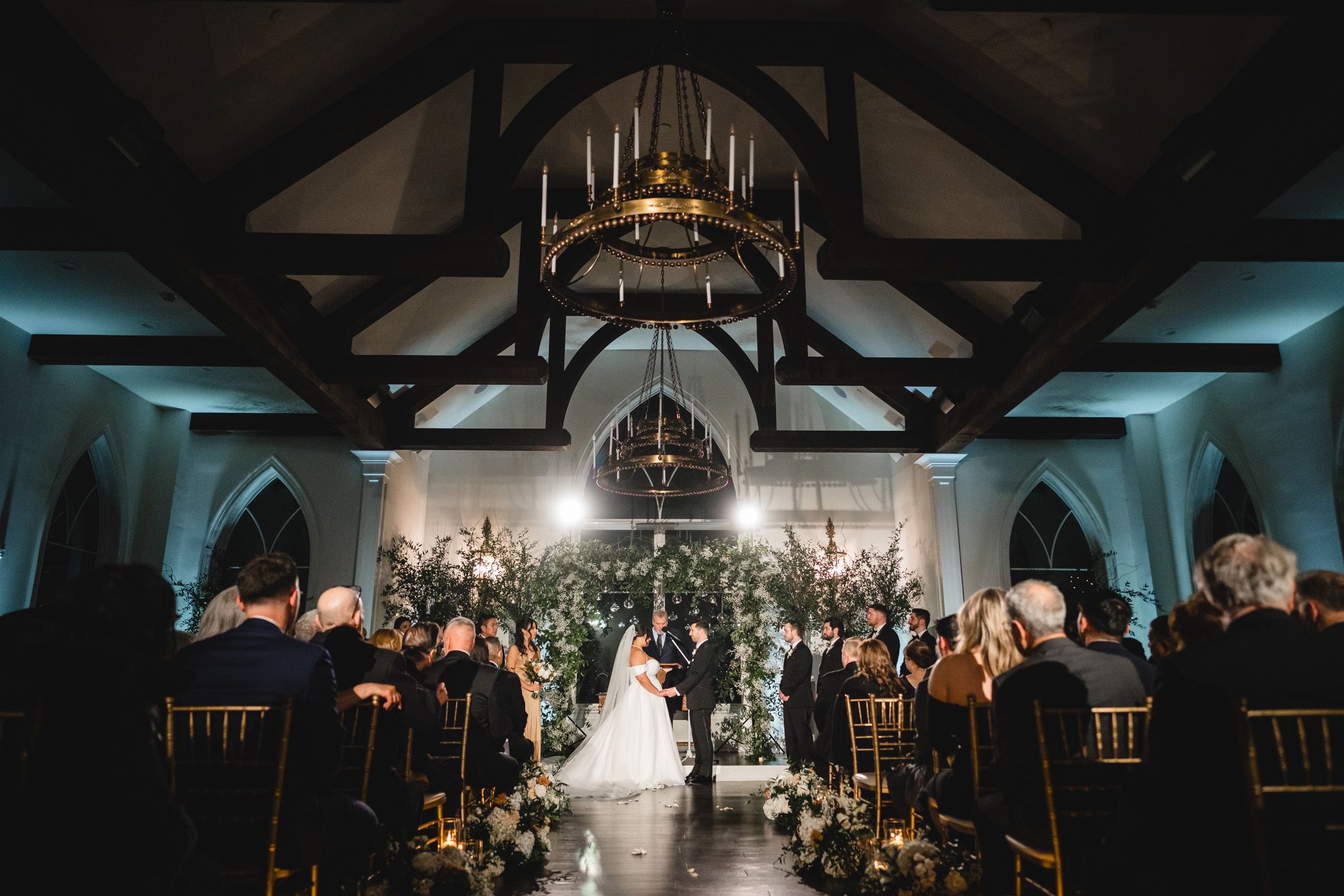 Dramatic church wedding ceremony with vaulted ceiling and candlelit aisle decorations.