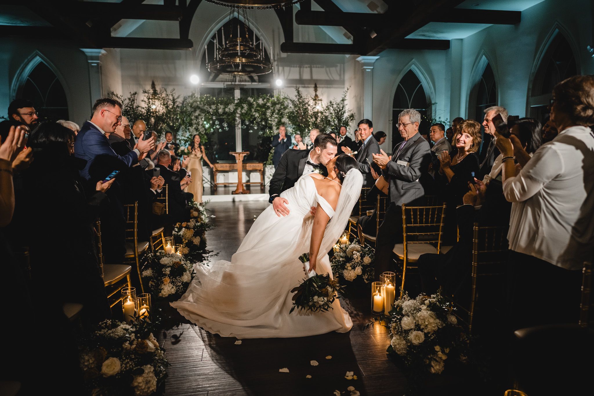 Wedding guests dance and celebrate on a dimly lit dance floor with romantic lighting and decorations.