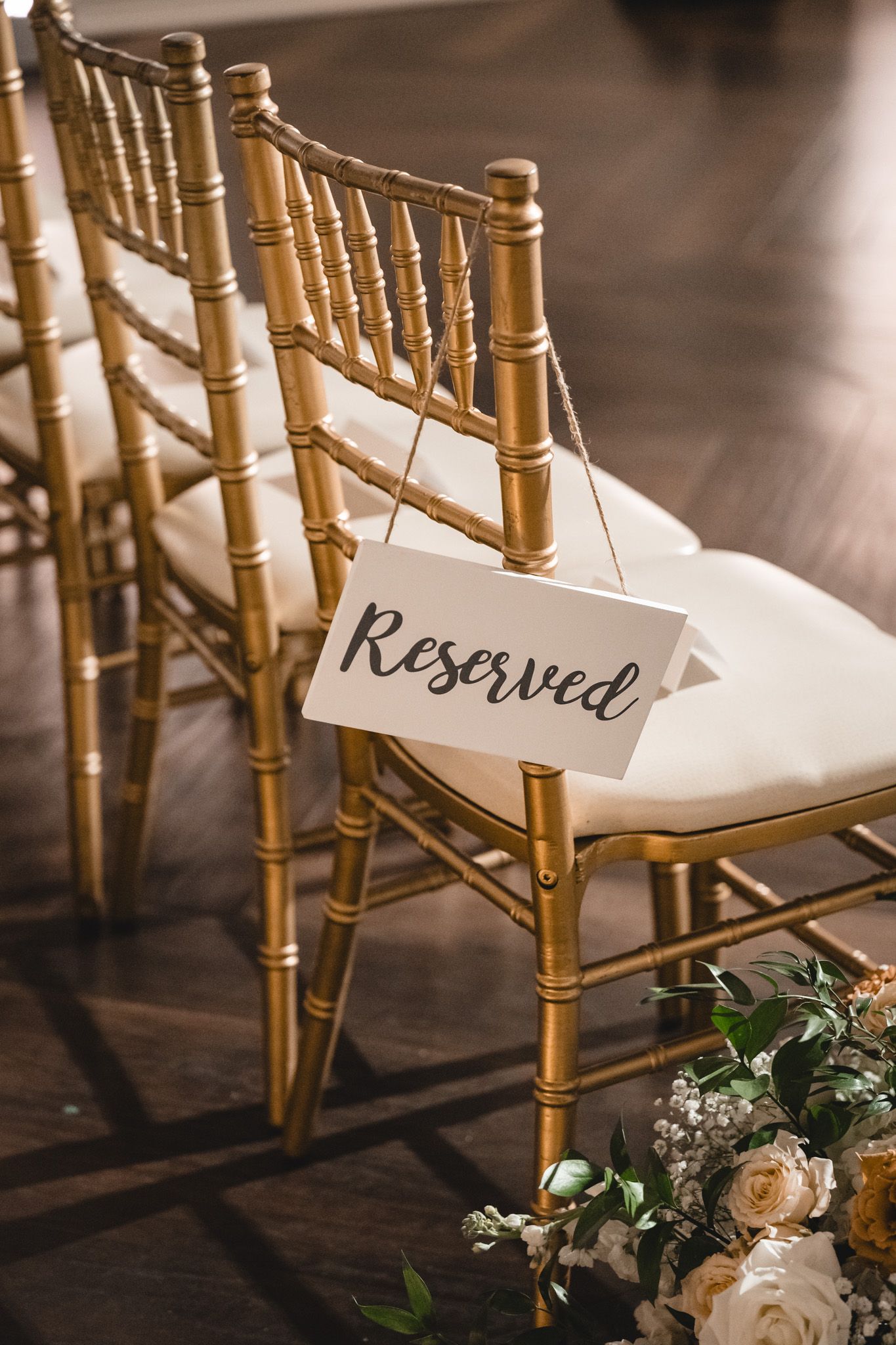 Gold chiavari chairs with reserved signs and floral decorations at wedding ceremony.