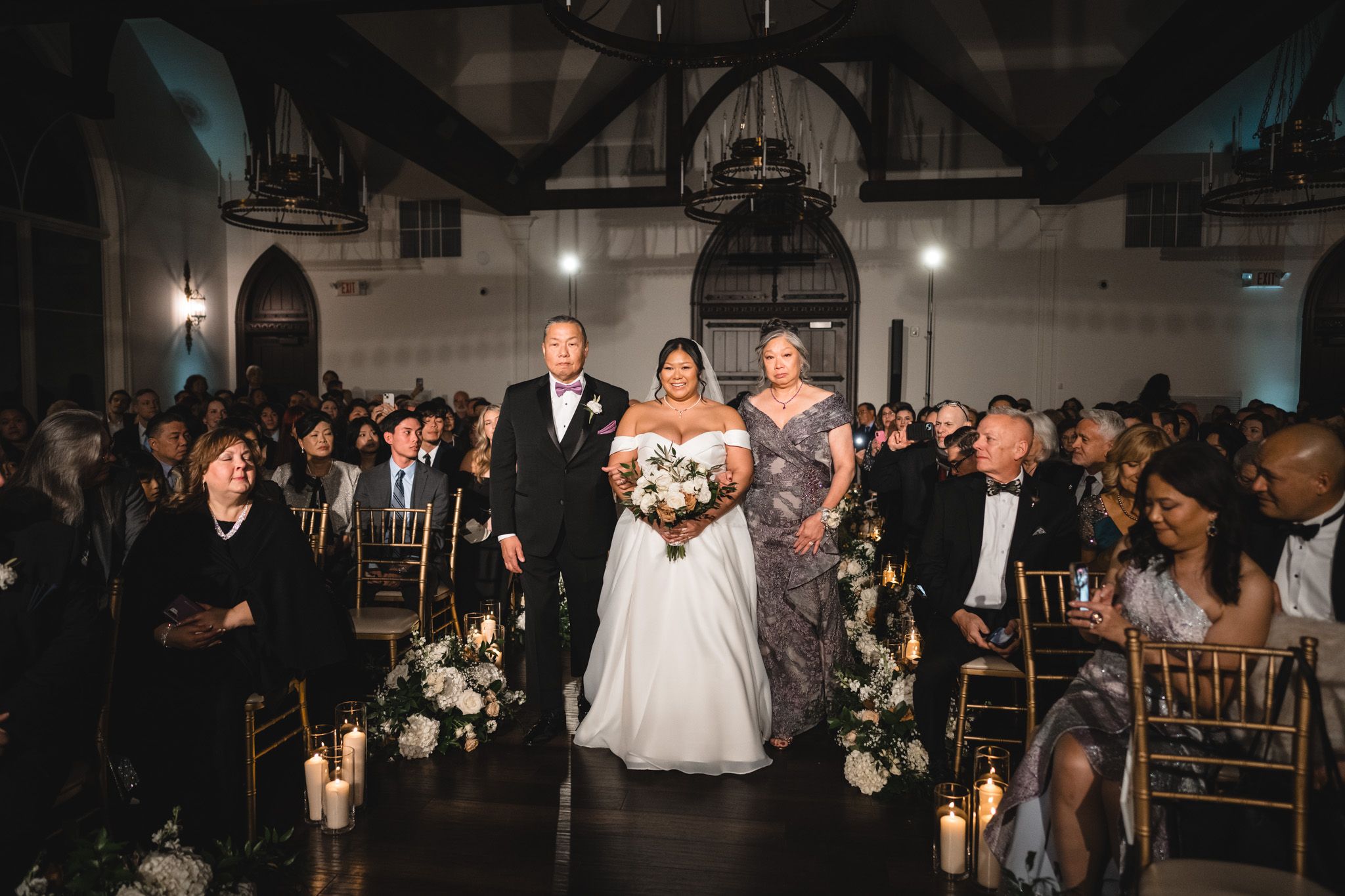 Indoor wedding ceremony with elegant floral decor and filled guest seating.