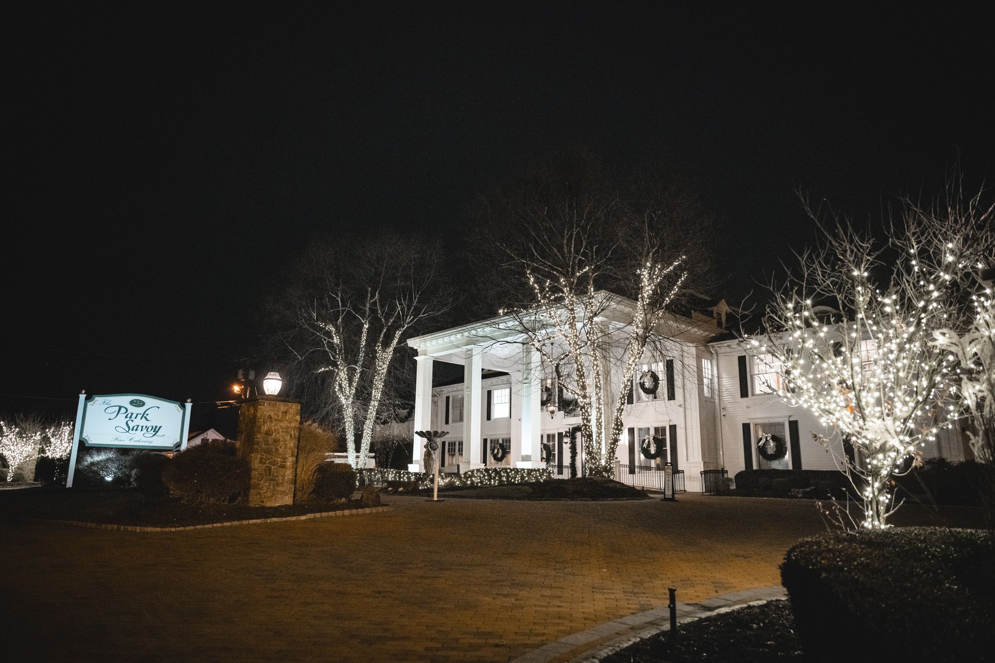 Exterior nighttime view of an elegant white building with illuminated trees and landscaping.