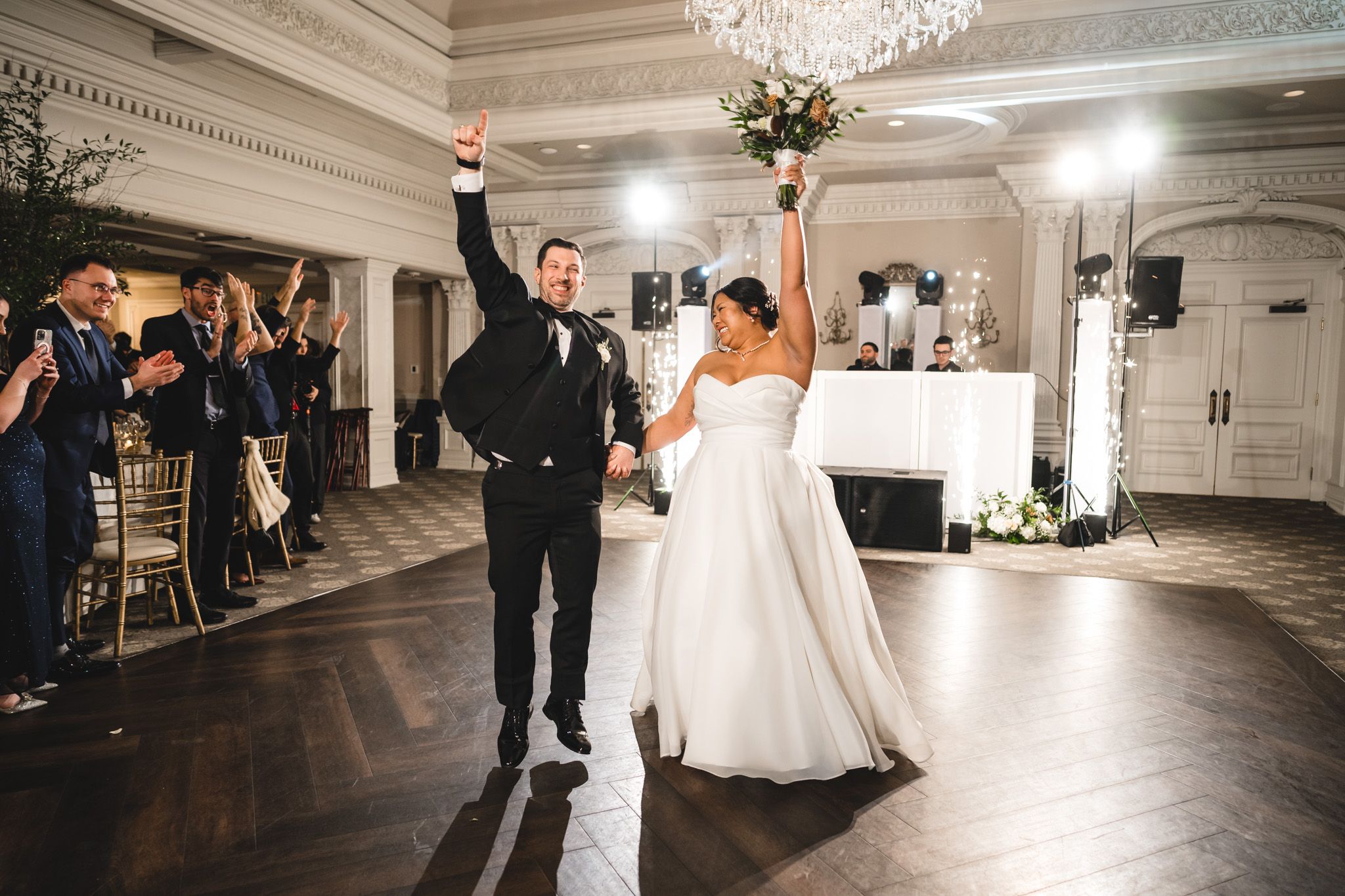 Couple dances in grand ballroom under ornate crystal chandelier during wedding reception.