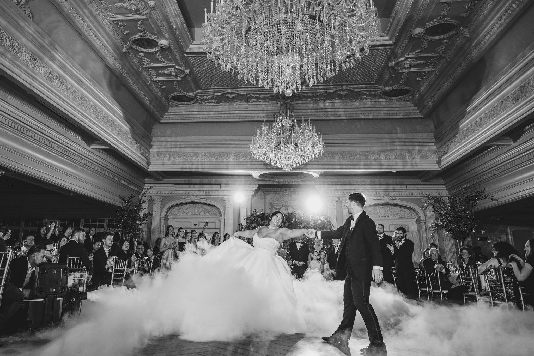 Dramatic black and white photo of first dance with fog effect in elegant ballroom setting.