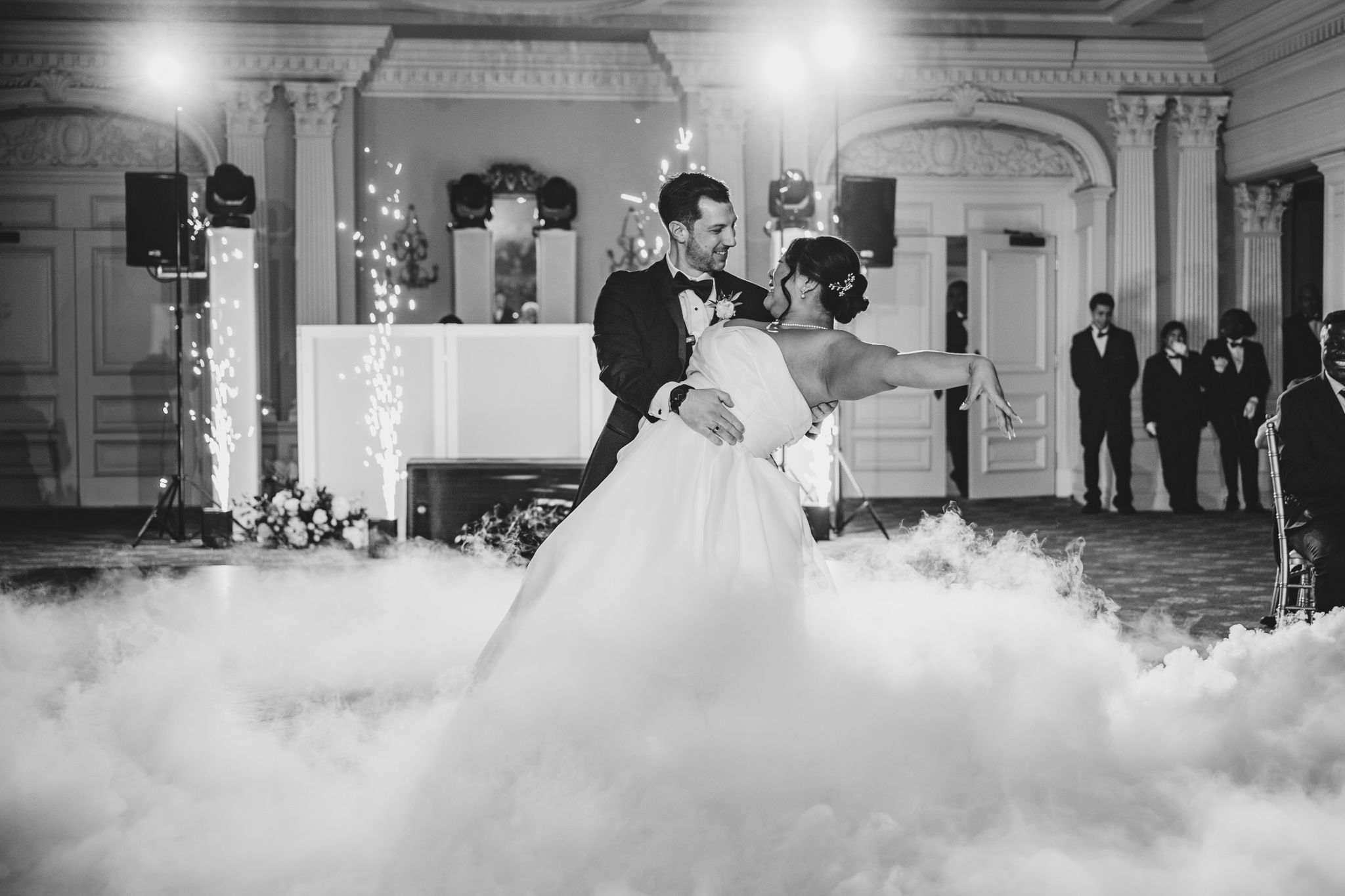Black and white capture of romantic dance with dramatic fog effect in elegant ballroom.