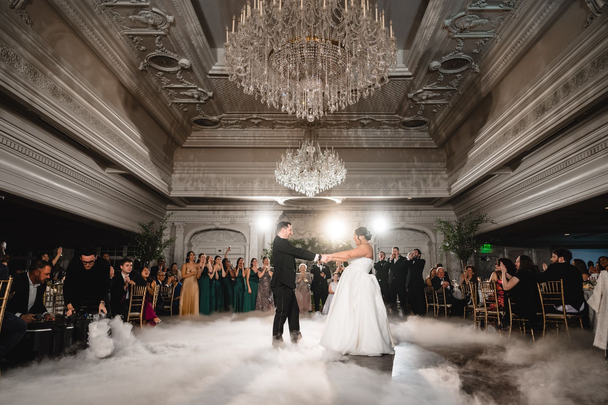 Wedding celebration in grand ballroom with low-lying fog effect and sparkling chandelier overhead.