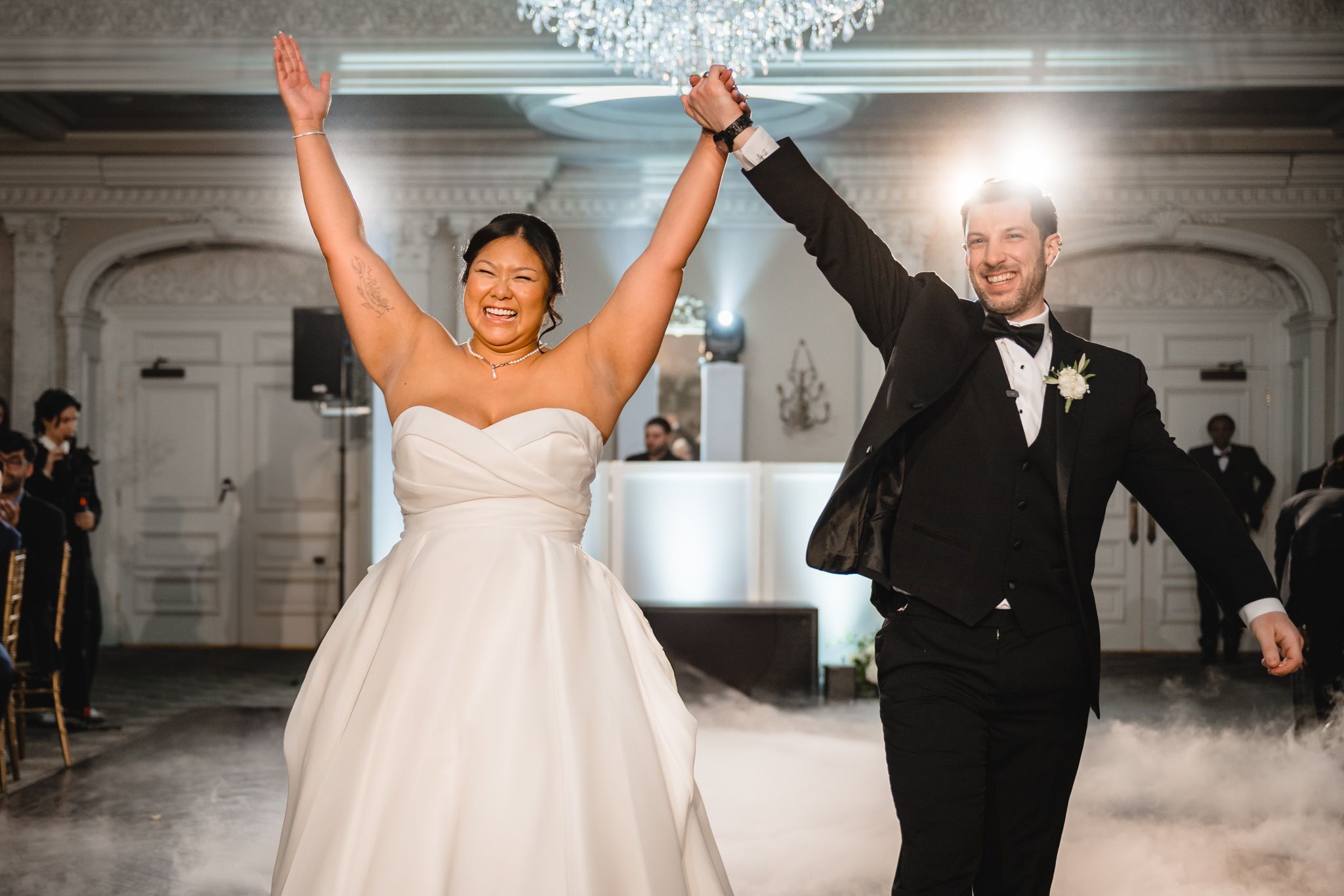 Joyful celebration moment during wedding reception in elegant chandelier-lit ballroom.