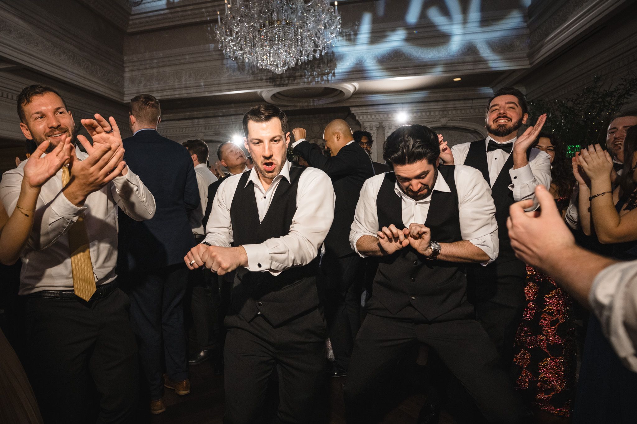 Wedding guests in formal attire dancing together at an elegant reception venue.