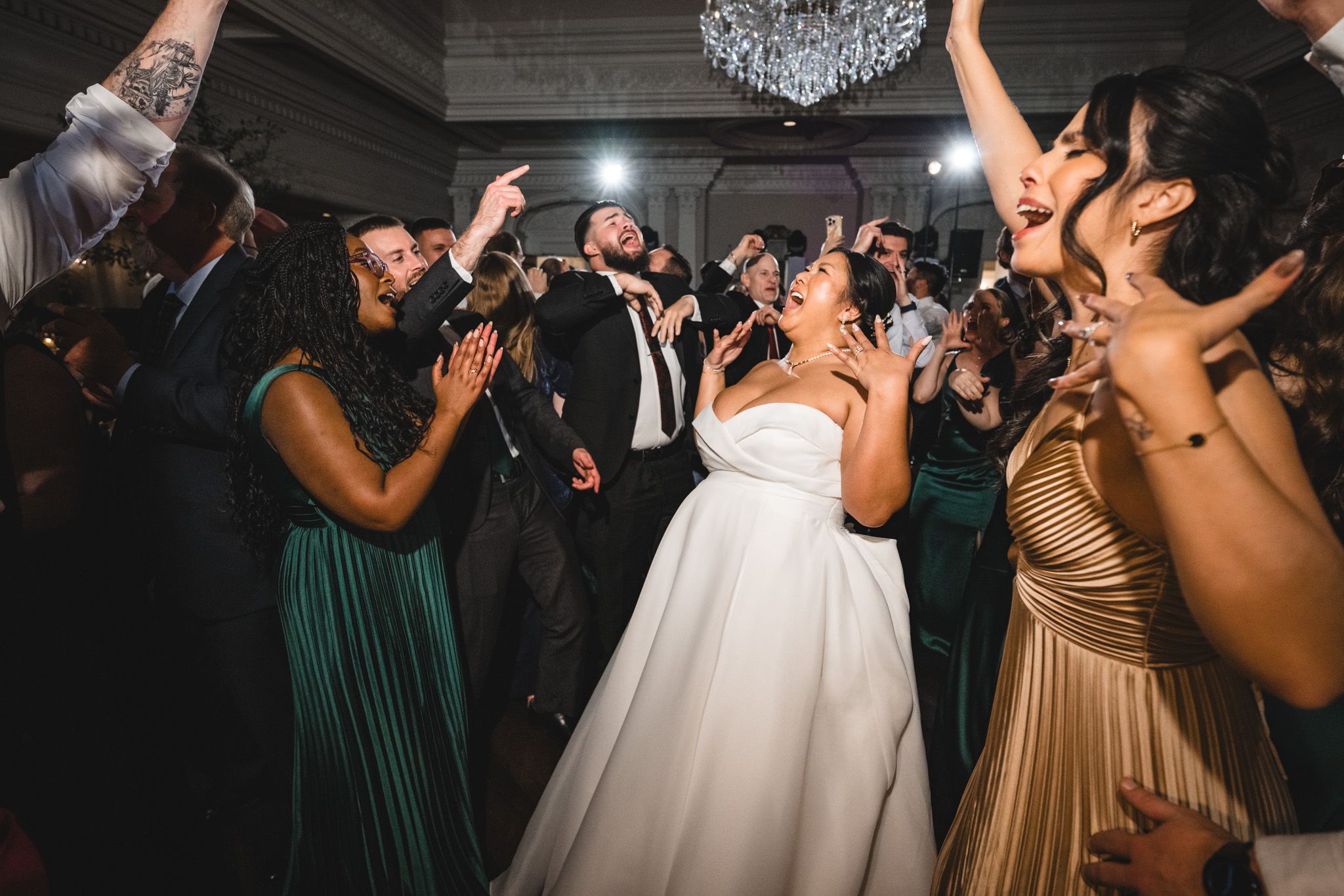 Wedding celebration with guests dancing enthusiastically under ornate chandeliers.