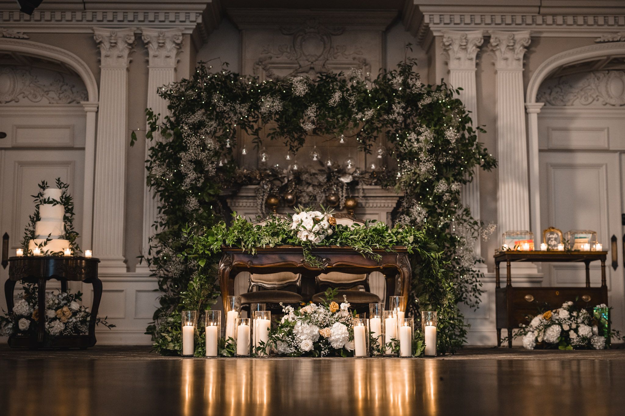 Ornate ballroom interior with decorative moldings, chandeliers and greenery accents.