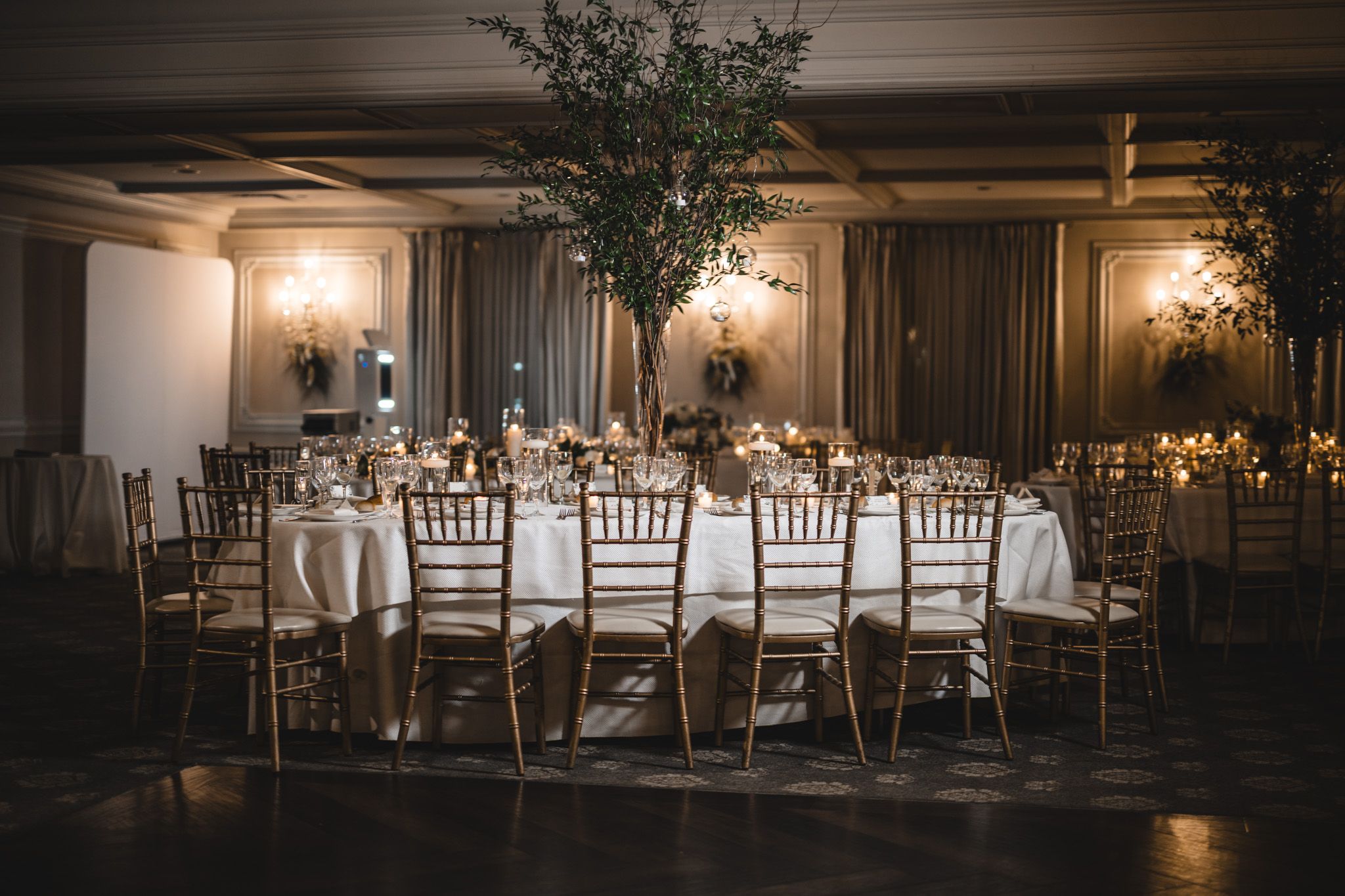 Elegant reception hall set with round dining tables and chiavari chairs in warm lighting.