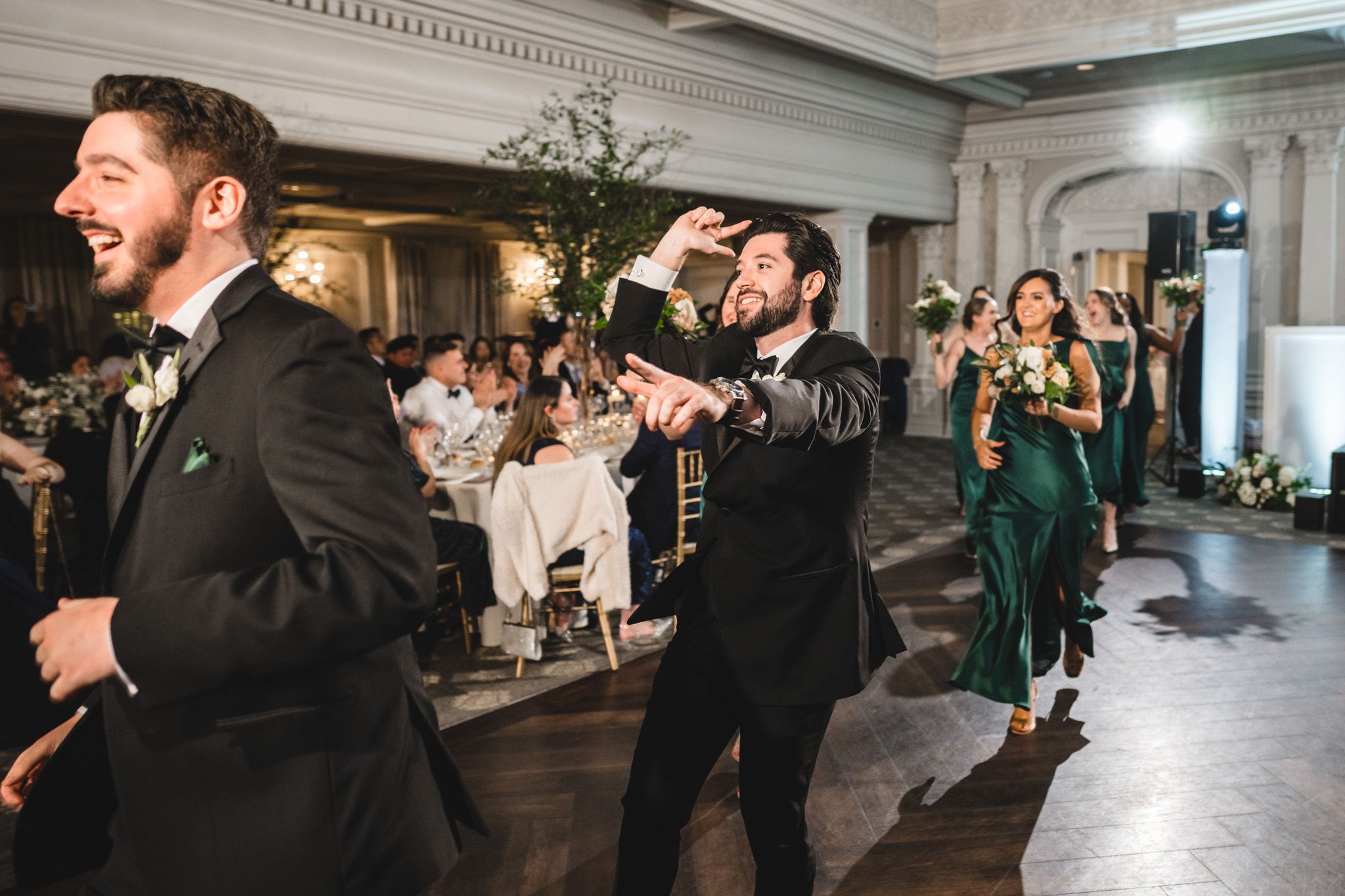 Wedding celebration with guests dancing in a grand ballroom with ornate architectural details.
