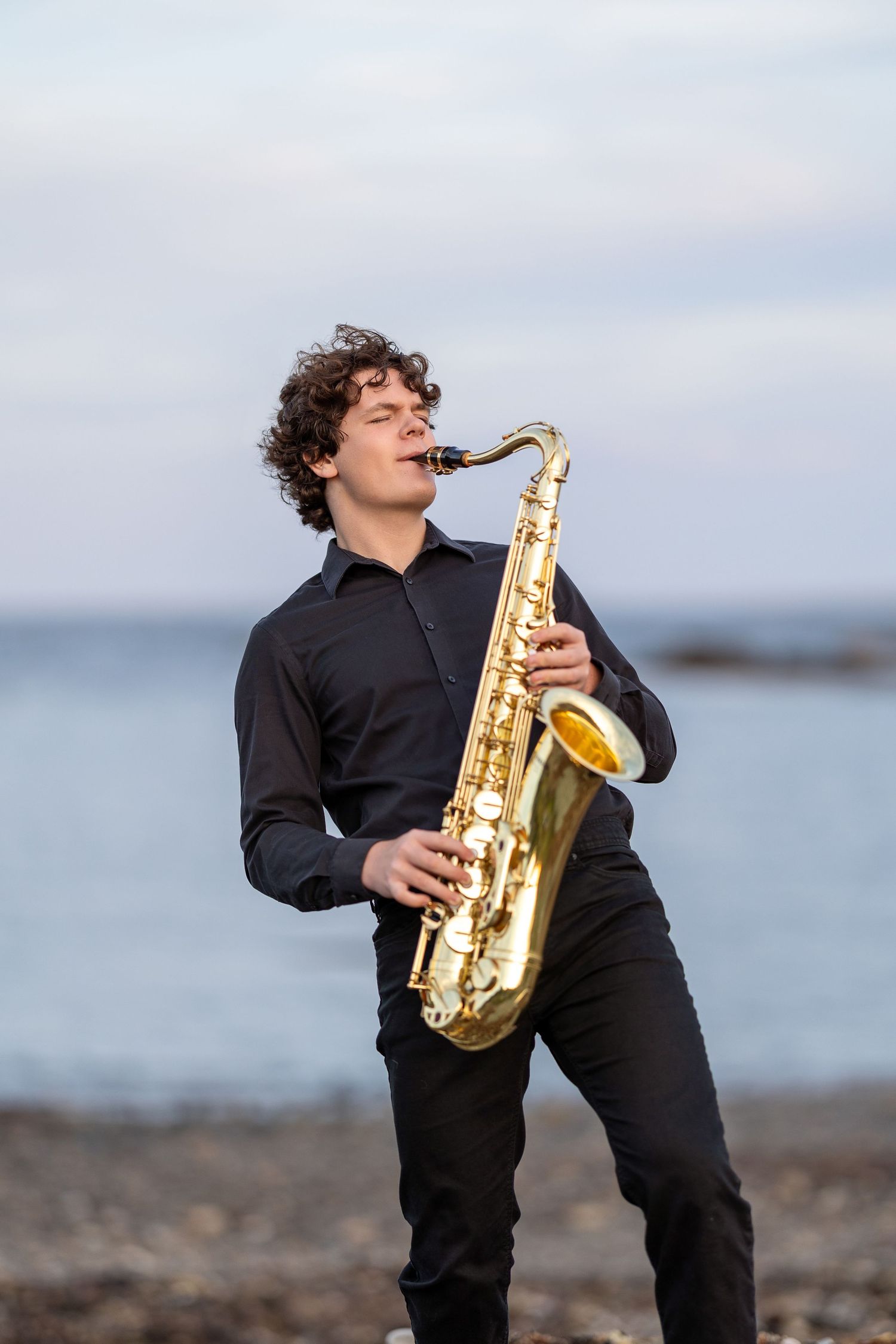 High school senior portrait playing the saxophone at the beach by the water in Rye NH