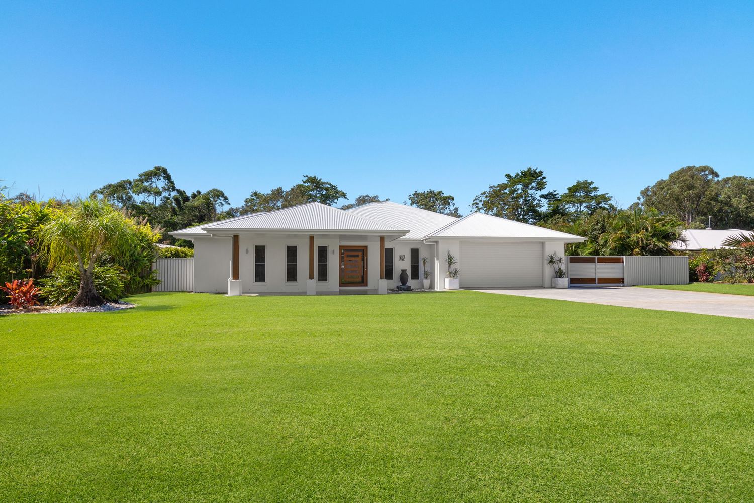 Spacious white single-story home with large green lawn and native trees under bright blue sky in Queensland Australia.