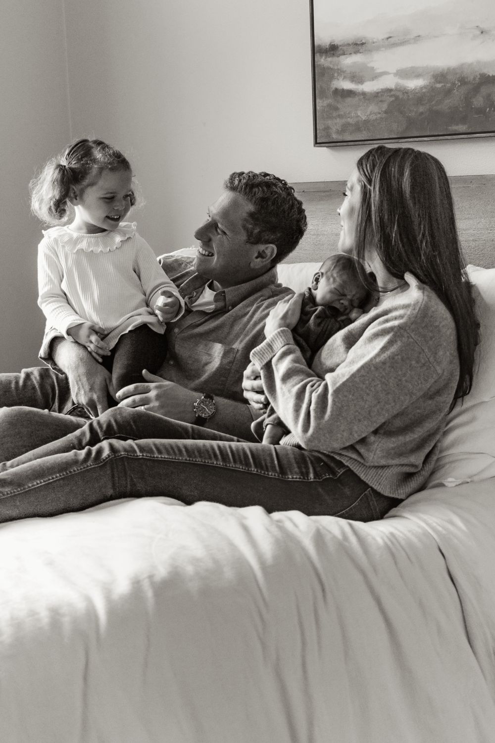 Candid black and white photo of family relaxing together on bed with infant.