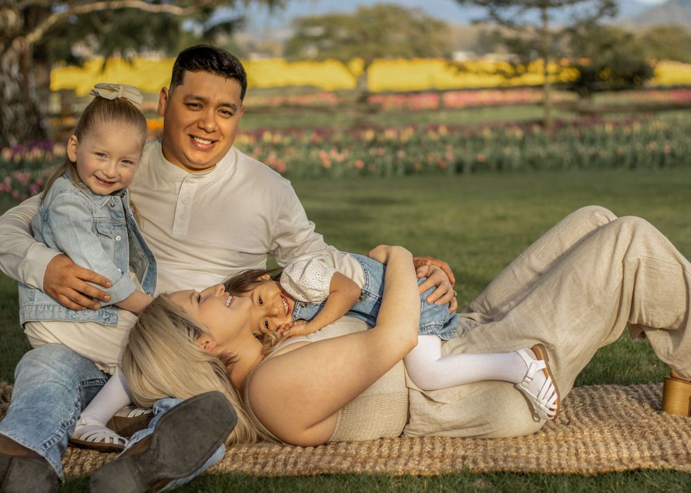 Family sharing tender moment while relaxing on blanket in outdoor setting.