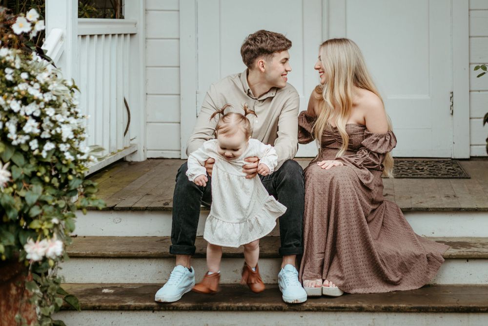 Family sitting together on white porch steps with blooming flowers in the background.