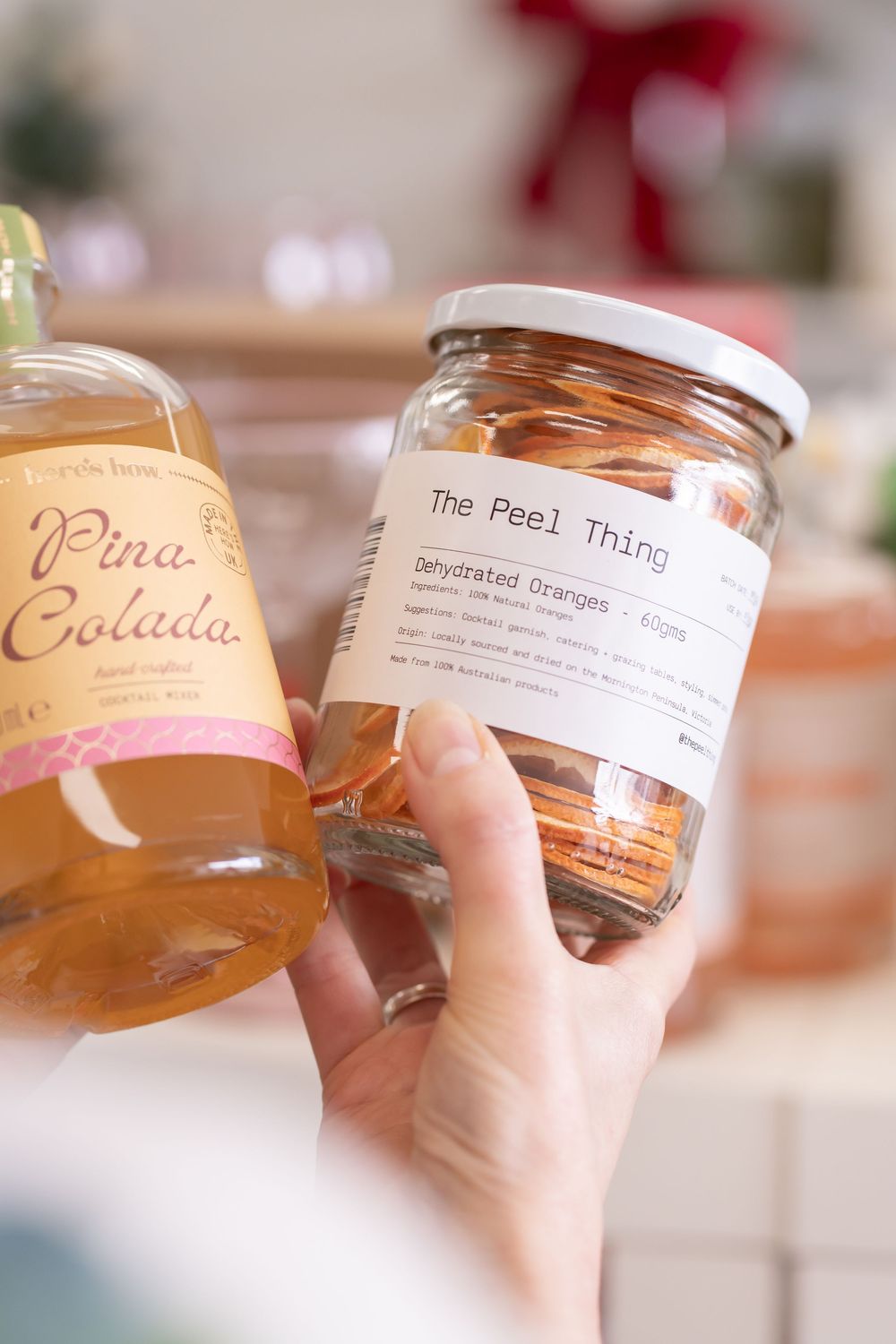 Hand holds glass jars with handwritten labels showing cocktail names Pina and Colada in warm lighting.