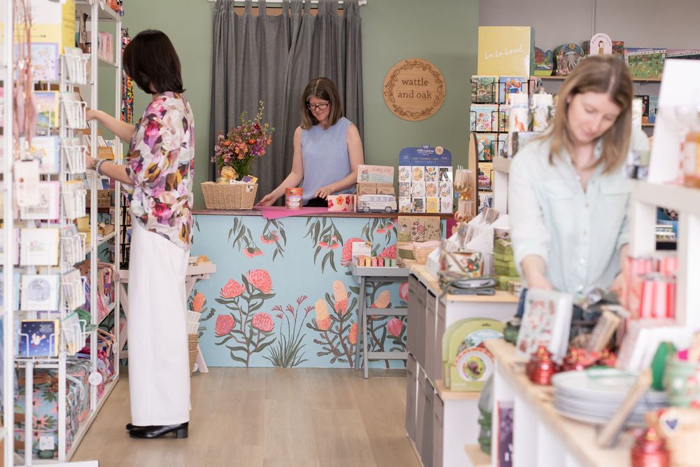 Retail shop interior with floral counter design, greeting cards display and customers browsing merchandise.