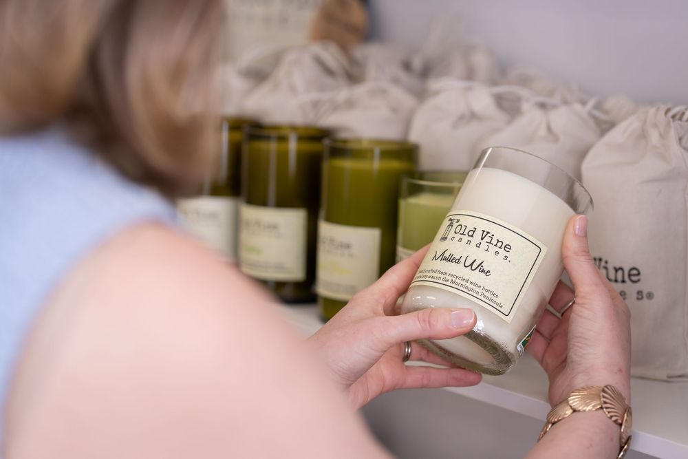 A person's hand holds a small white candle jar with a minimalist label design against a blurred background.