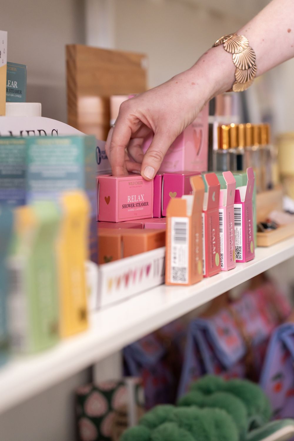 Hands arranging pink product boxes on white retail shelves with colorful merchandise in the background.