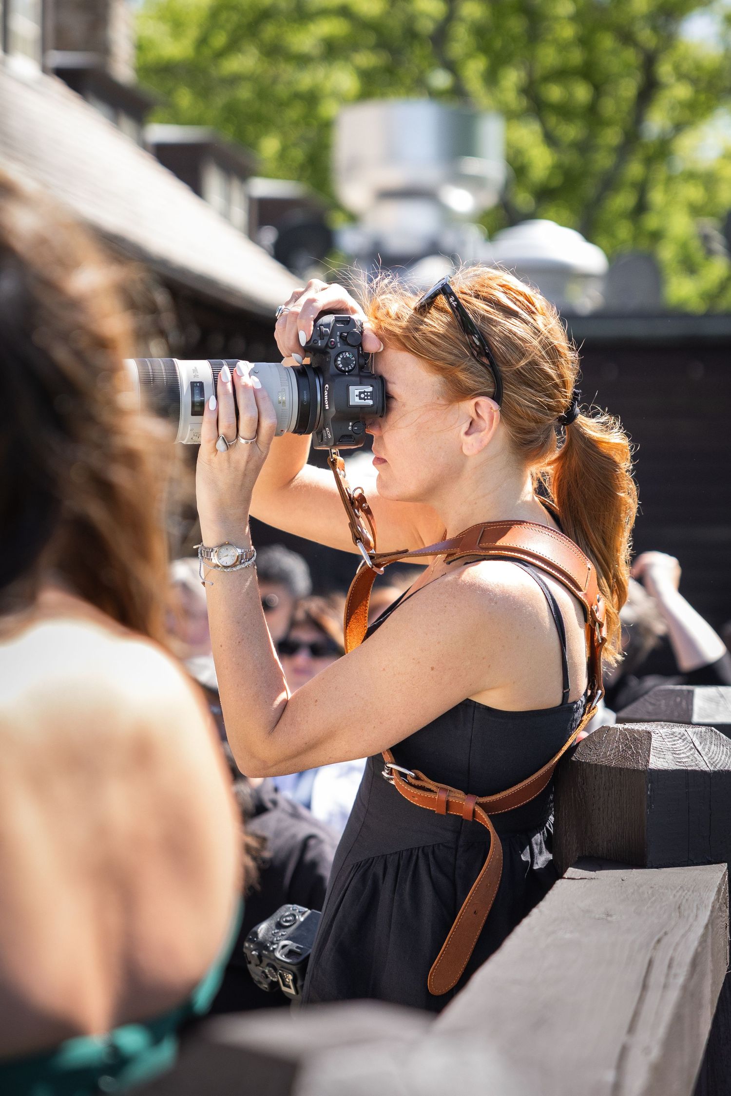 Woman with red hair photographing with DSLR camera and telephoto lens outdoors on a sunny day.