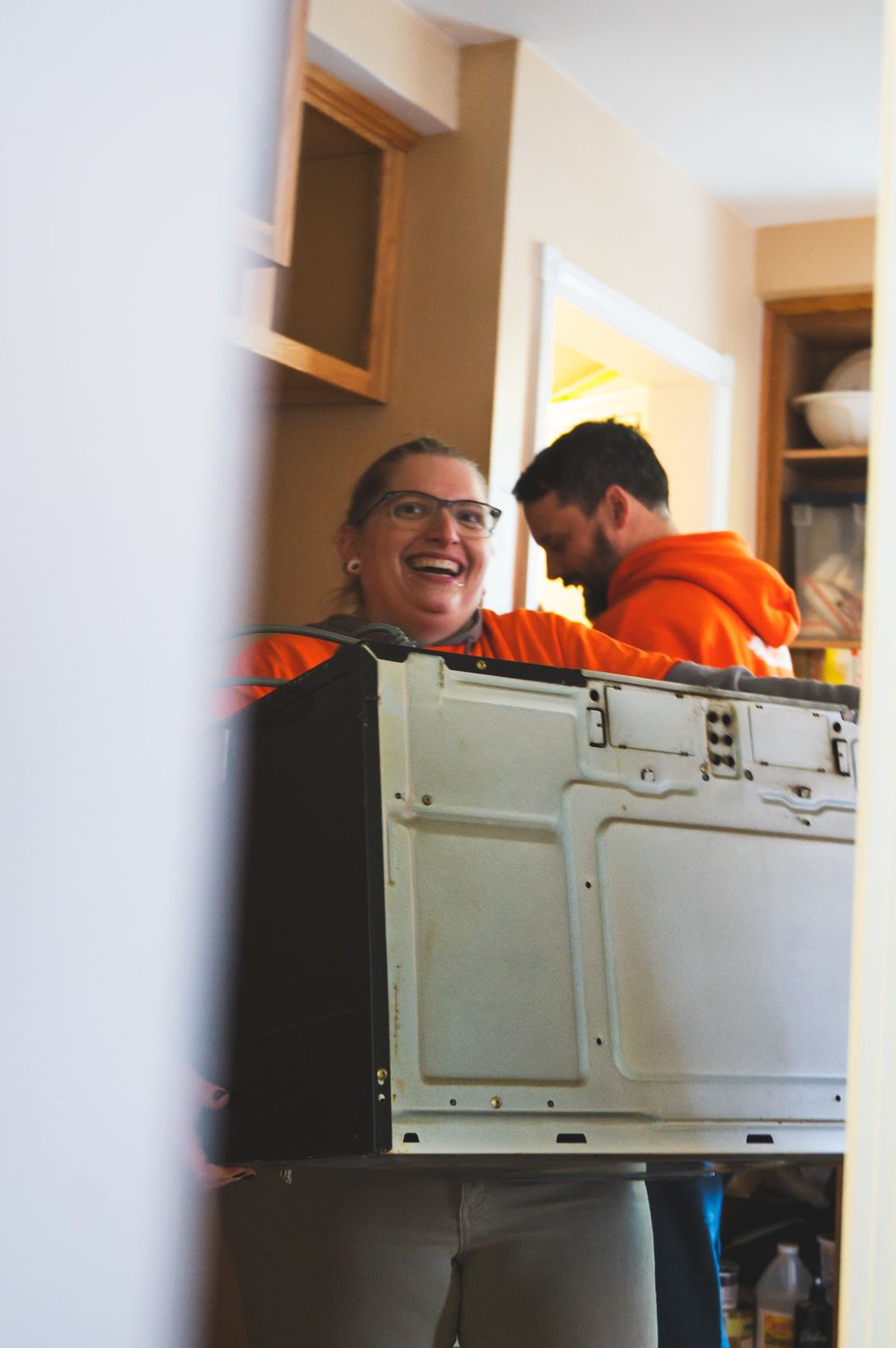 People in orange clothing work behind a white computer tower or equipment case in an indoor setting.