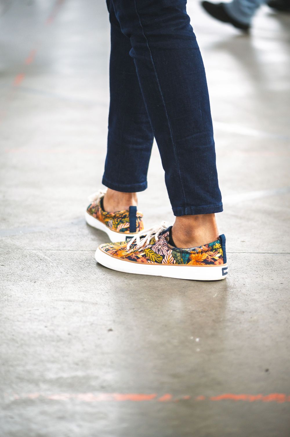 Close-up view of feet wearing colorful floral print slip-on sneakers with navy blue pants.