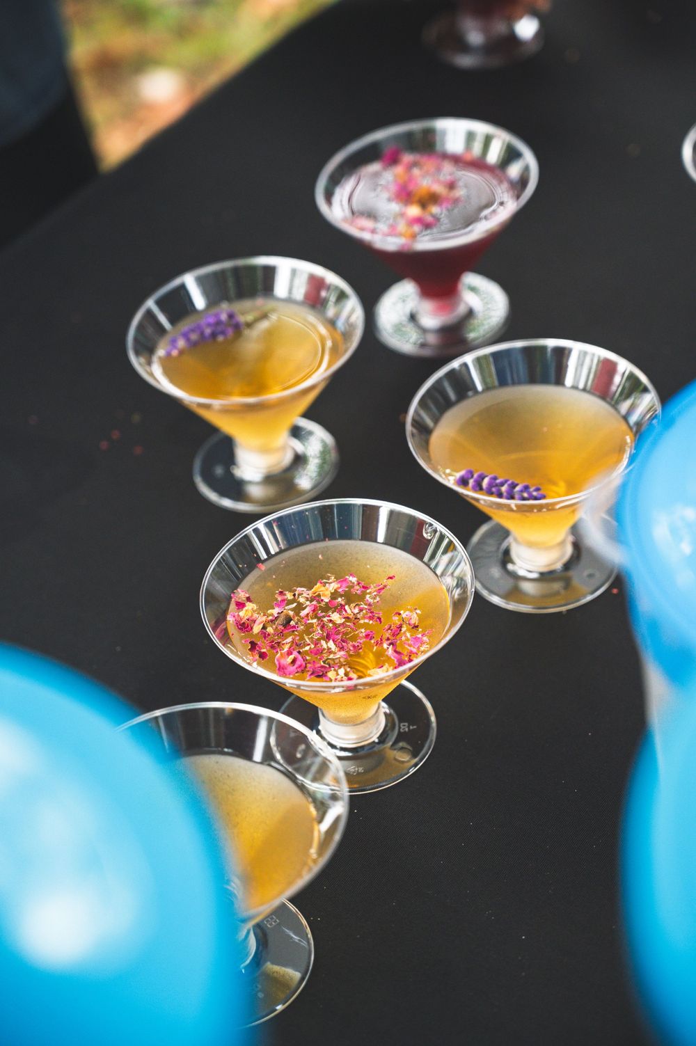 Cocktail glasses filled with orange liquid and colorful sprinkles on a dark surface with blue decor in background.