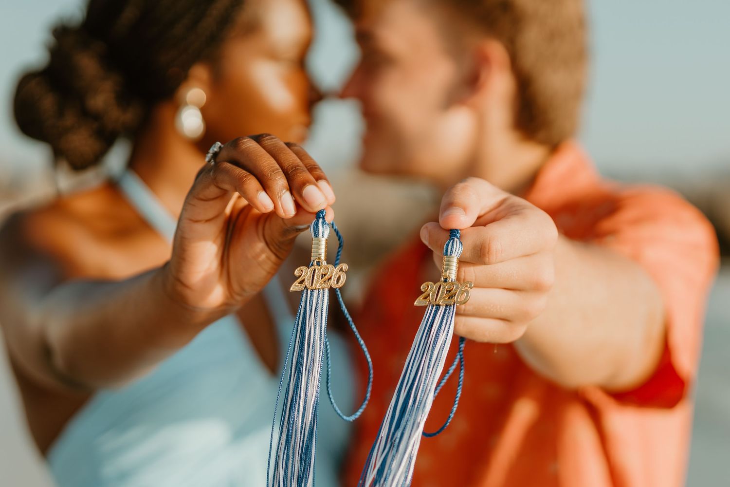 Close-up view of hands holding blue tassels for graduation ceremony against light background.