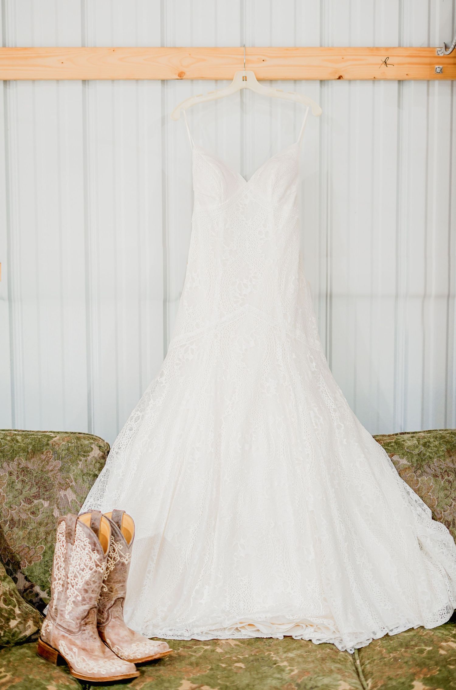 A white wedding dress and cowboy boots hanging against a metal wall.