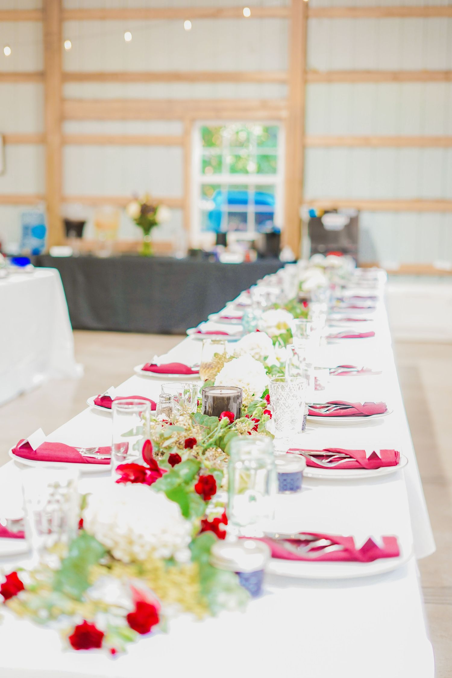 Elegant wedding reception table with white linens, pink napkins and floral centerpieces arranged in a long line.