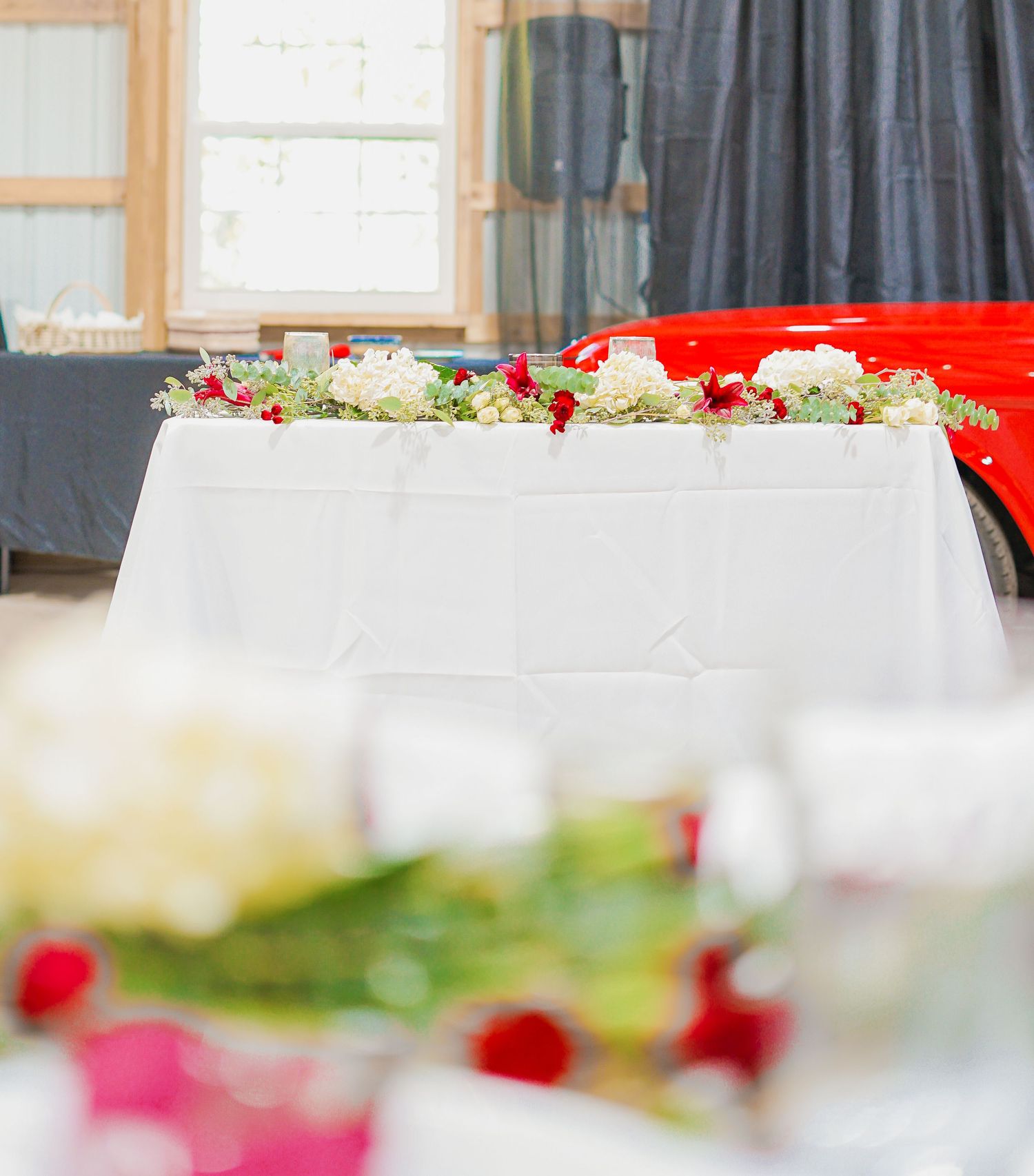 Close up of wedding table decor with white linens and red floral arrangements.
