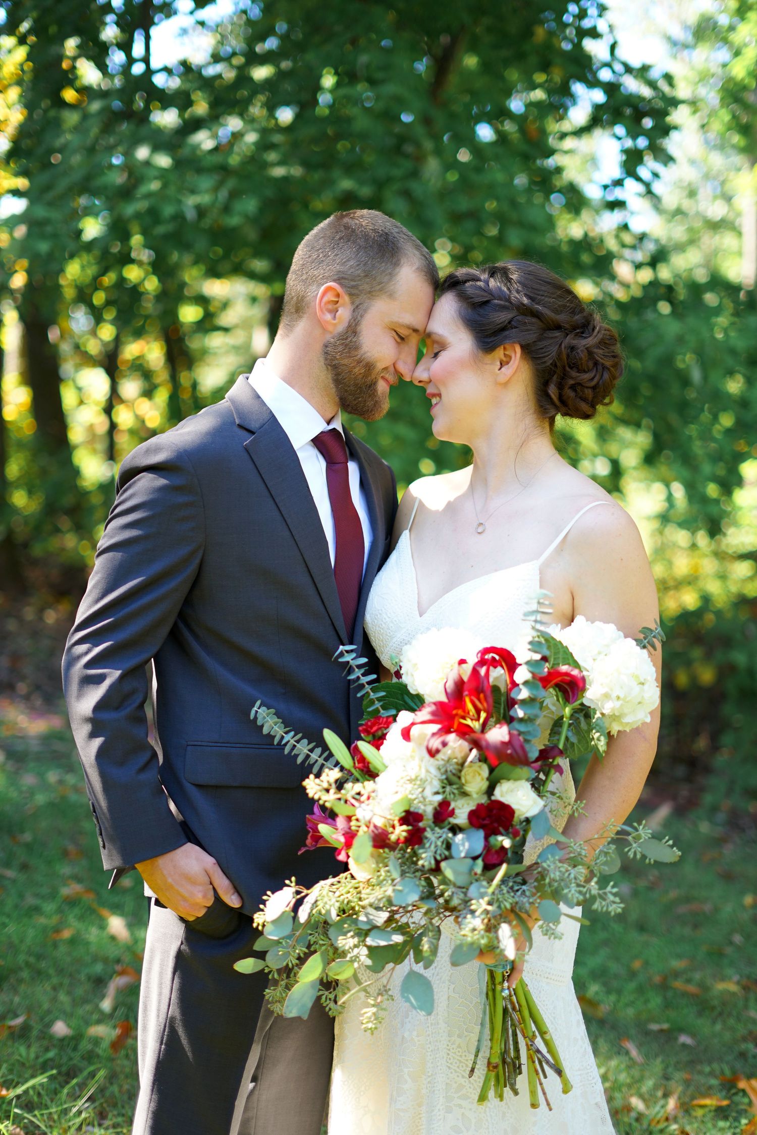 Romantic outdoor wedding portrait with red and white bouquet in a garden setting.