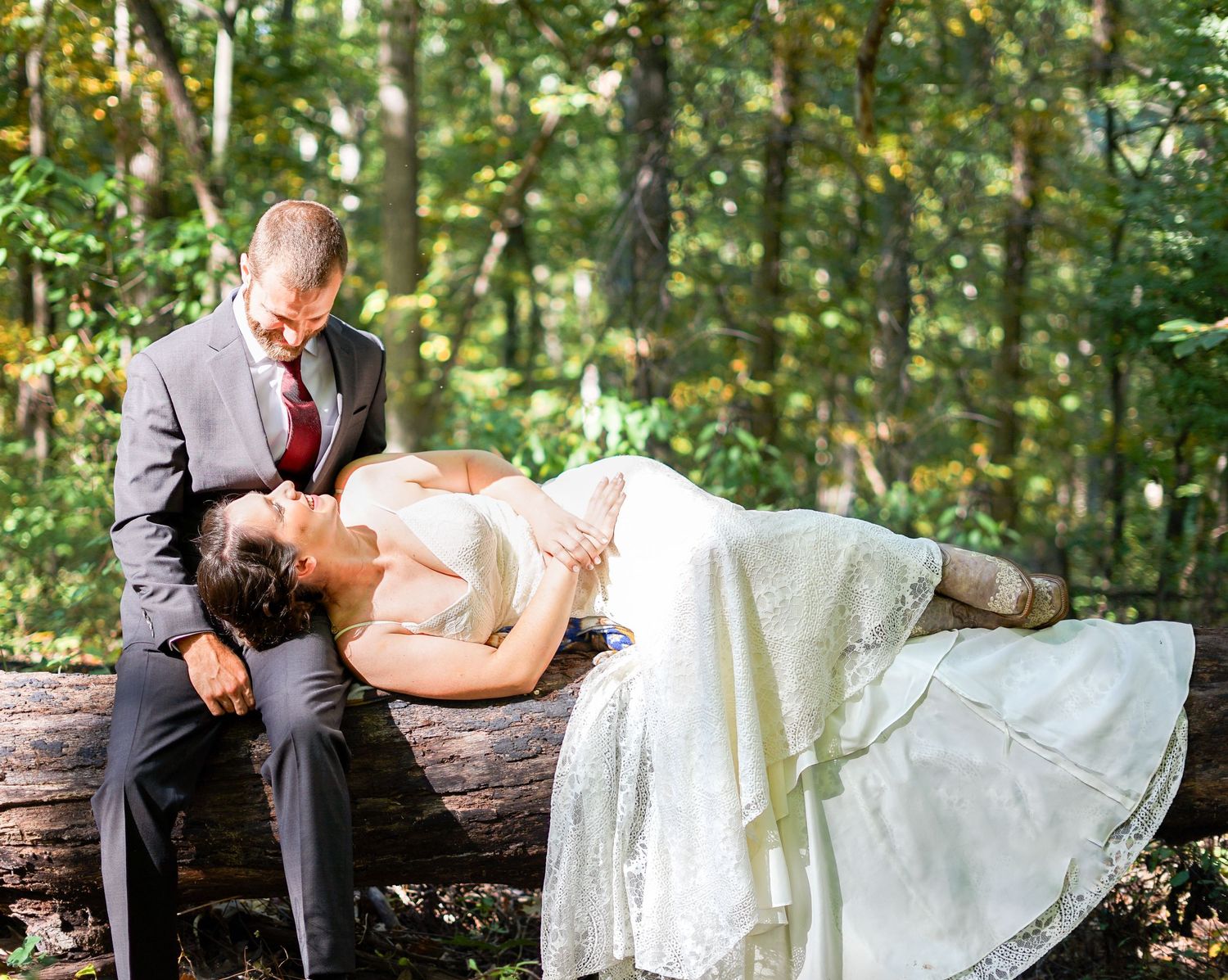 Artistic wedding photo of a couple posing on a fallen log in a forest setting.