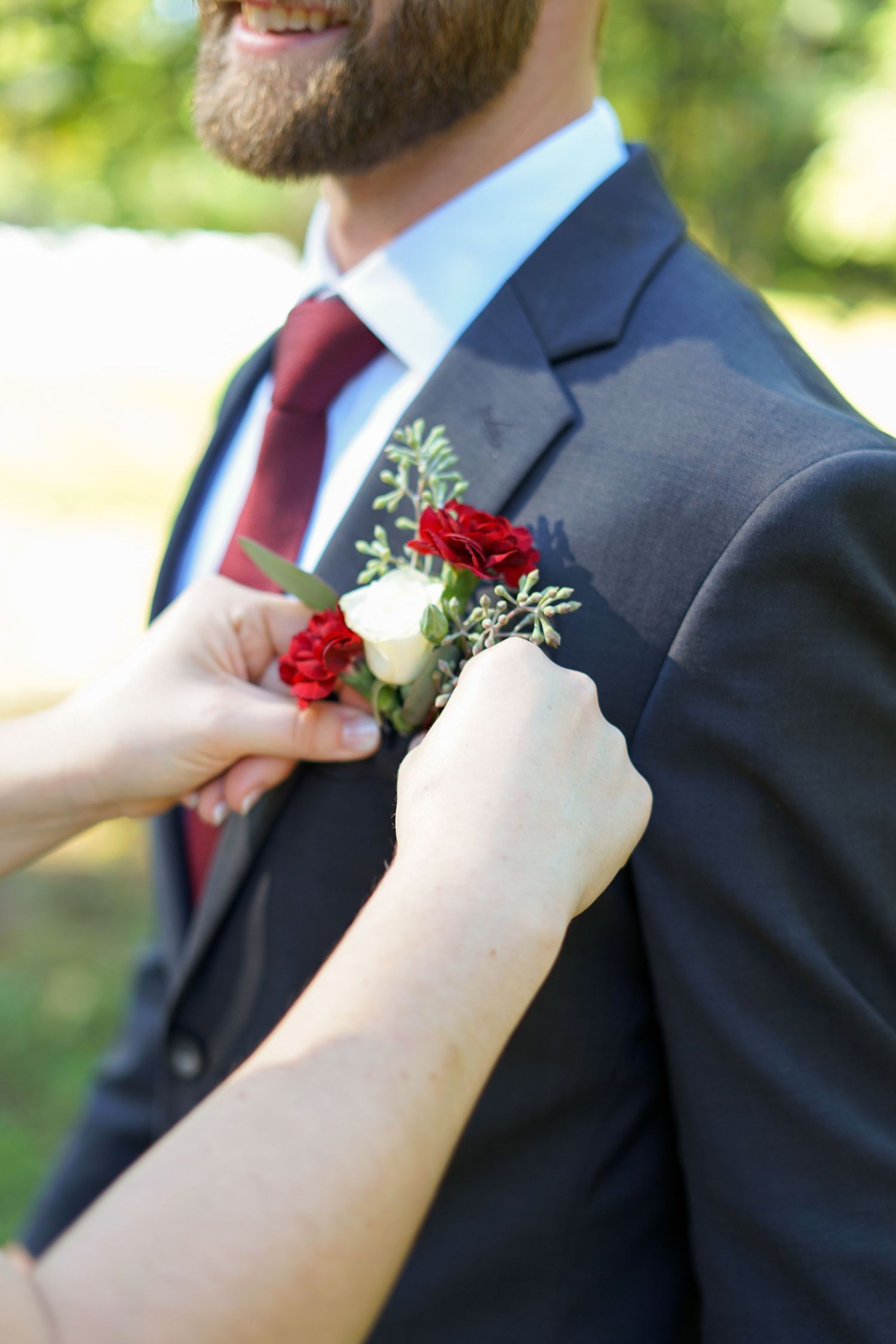 Hands pinning a red and white boutonniere onto a navy suit jacket.
