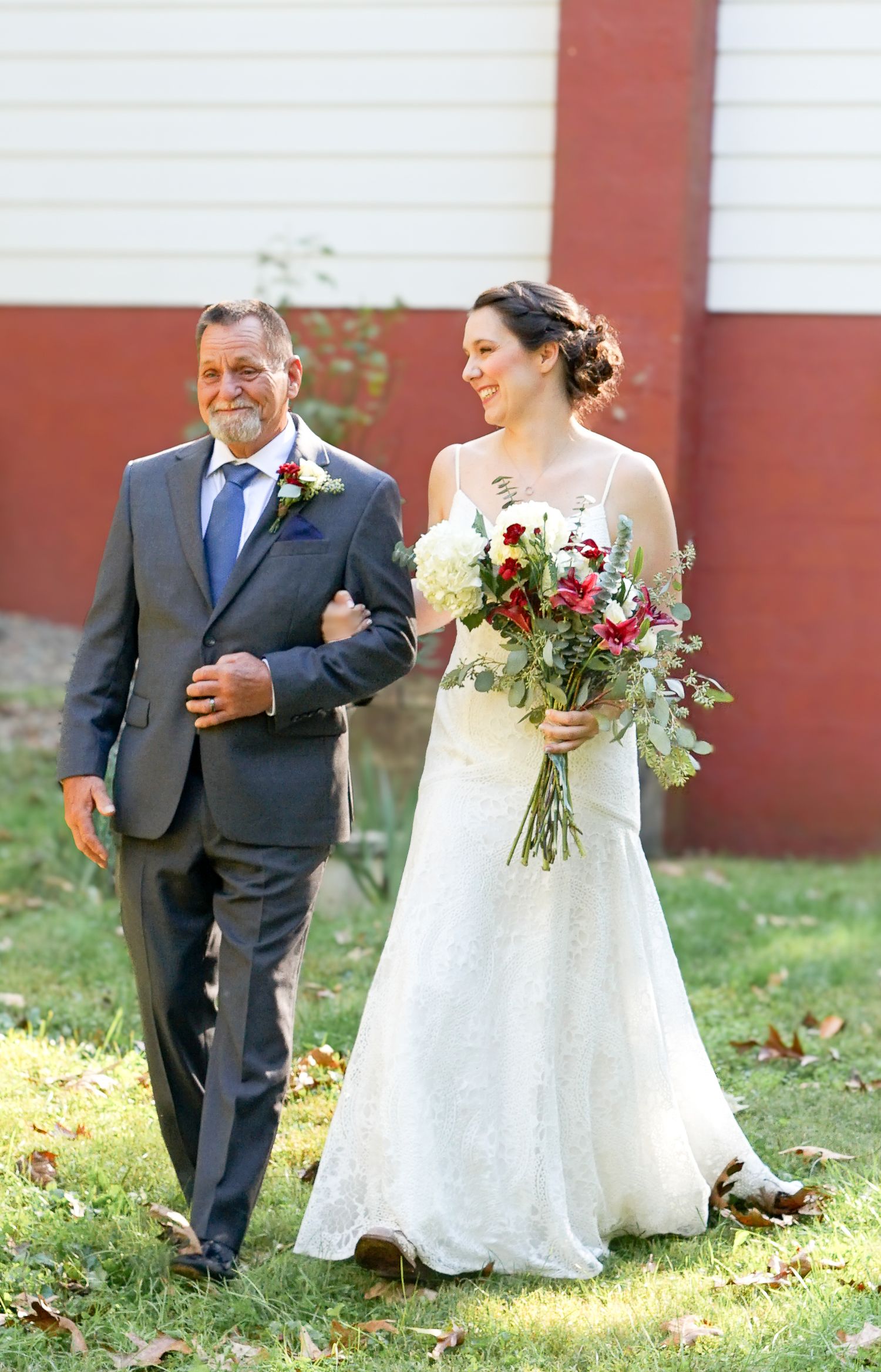 Wedding procession outdoors with elegant white dress and red brick building in background.