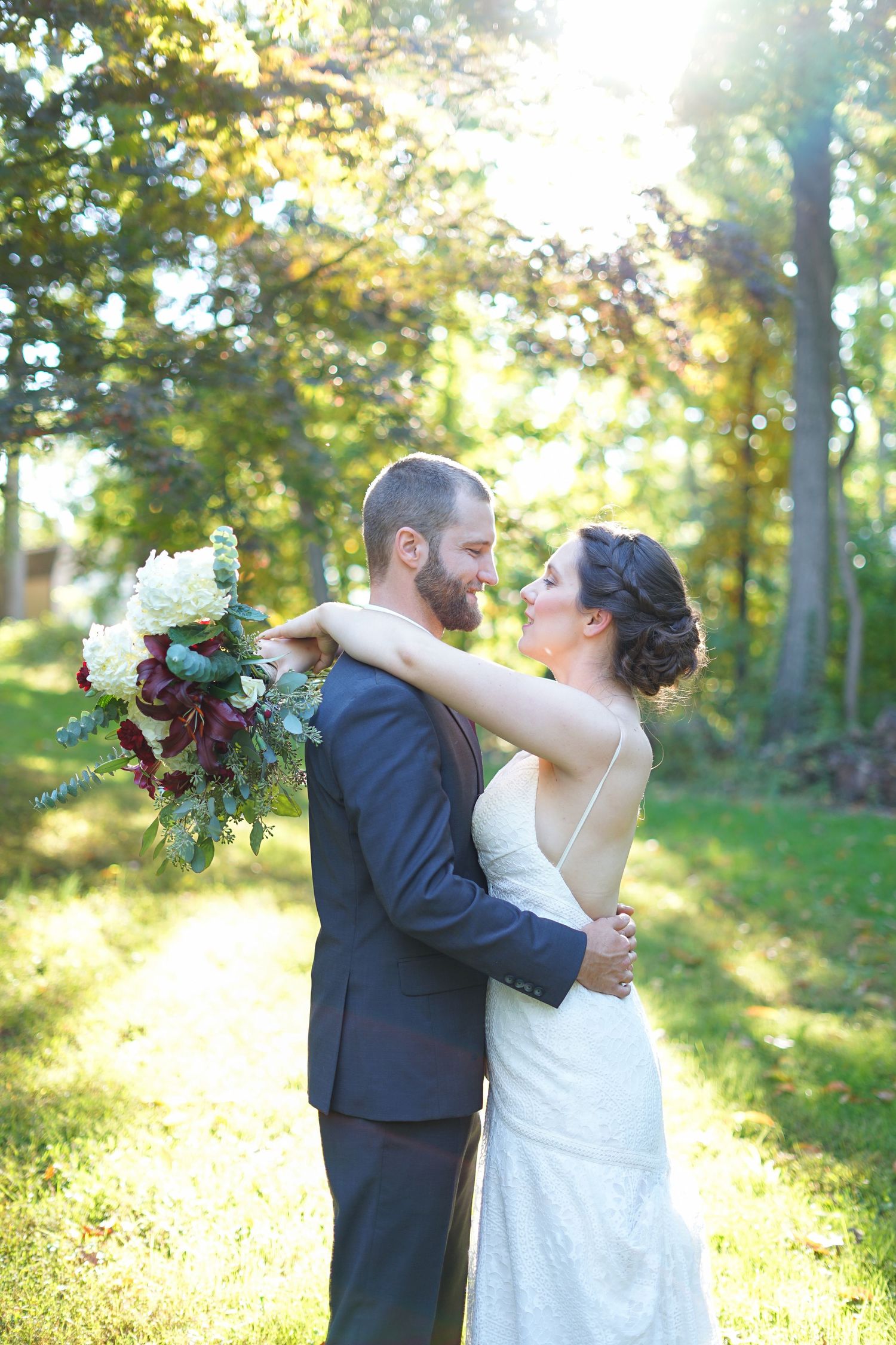 Sun-drenched wedding portrait with couple embracing in a wooded setting.