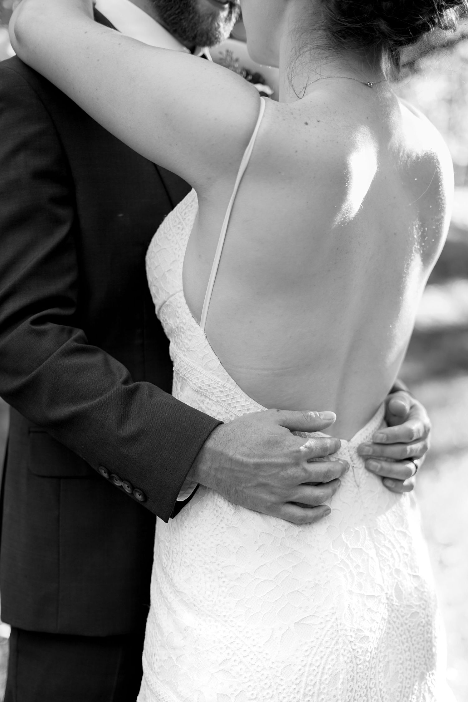 Intimate black and white detail shot of coupled embracing, focusing on the dress details.