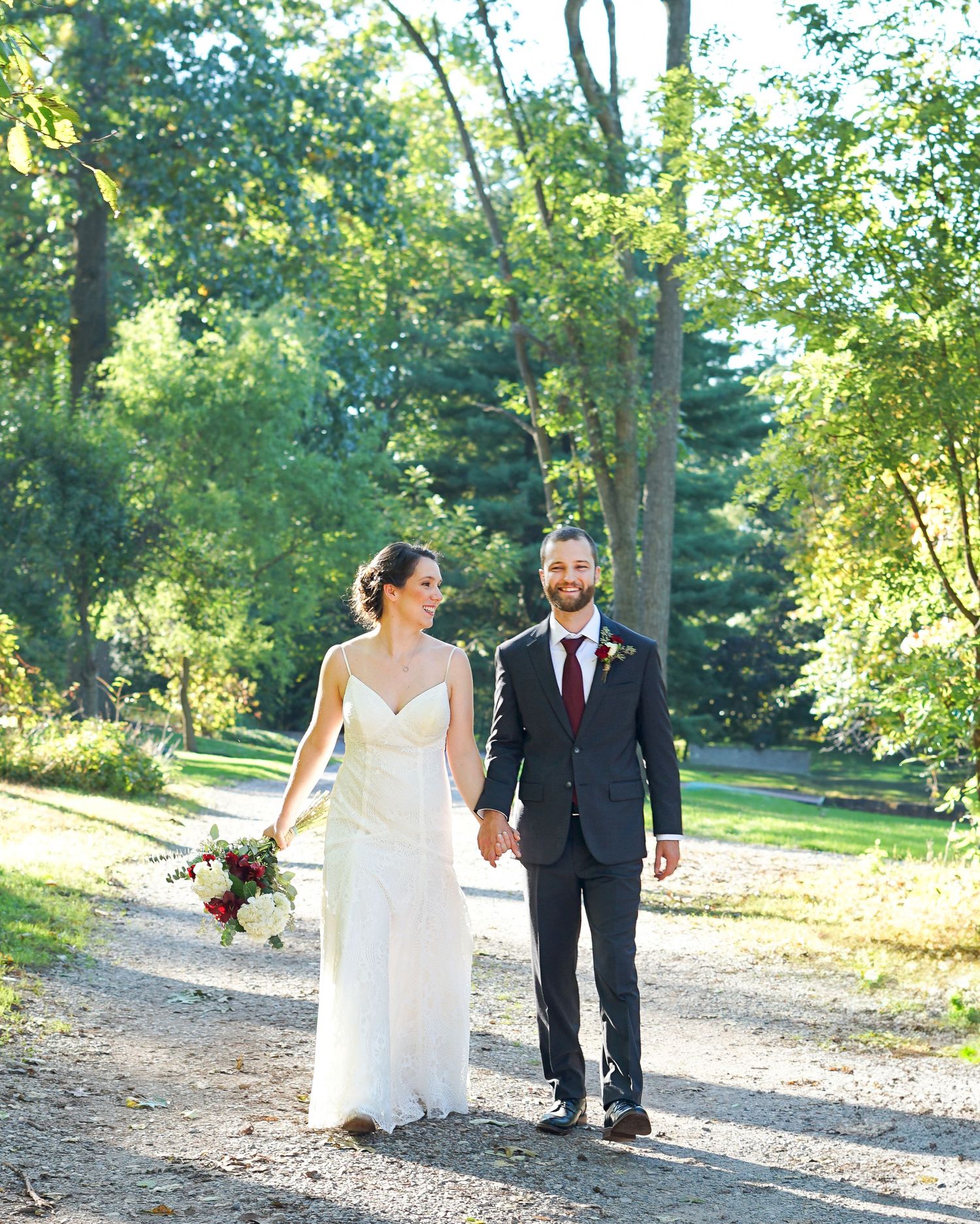 Couple walking hand in hand down a tree-lined path in wedding attire.