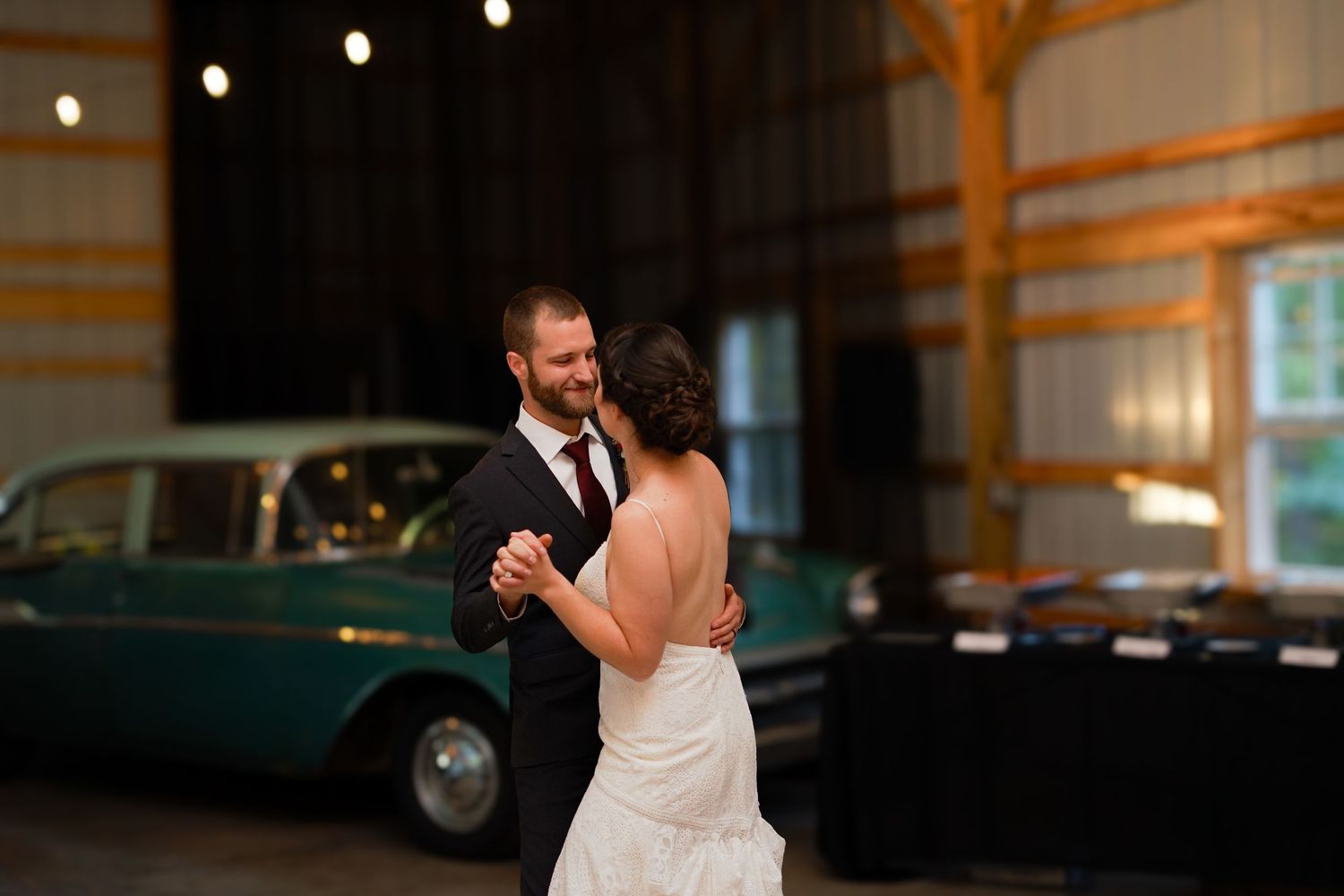 A romantic dance moment captured in a barn setting with a vintage car in the background.