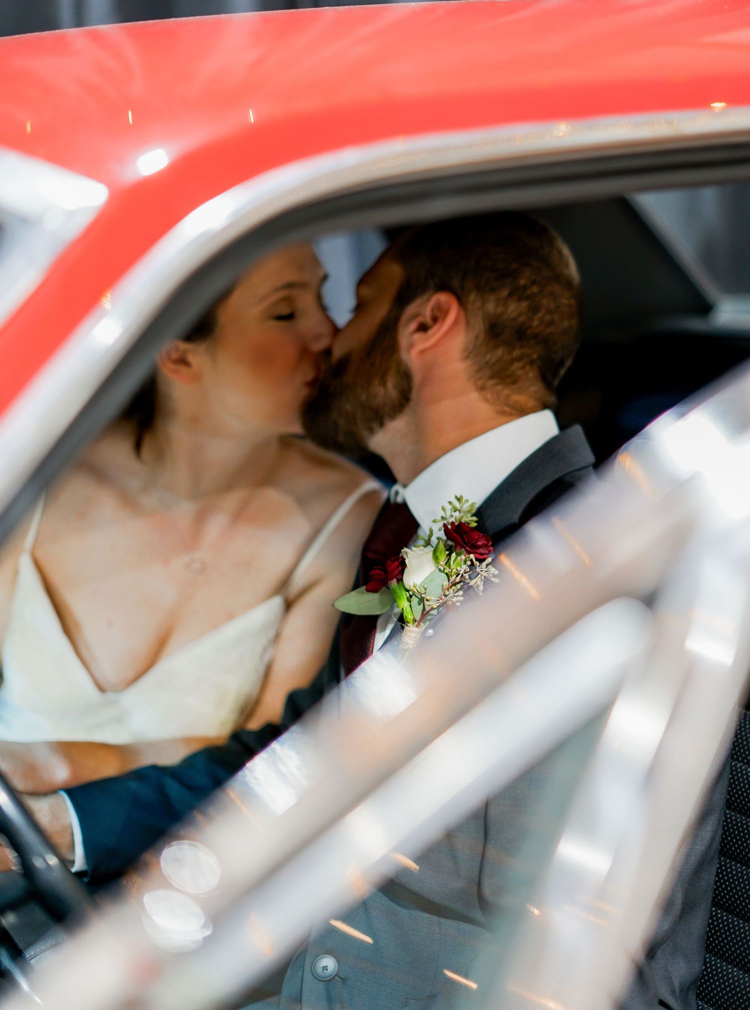 A tender moment shared in a red car on a wedding day.