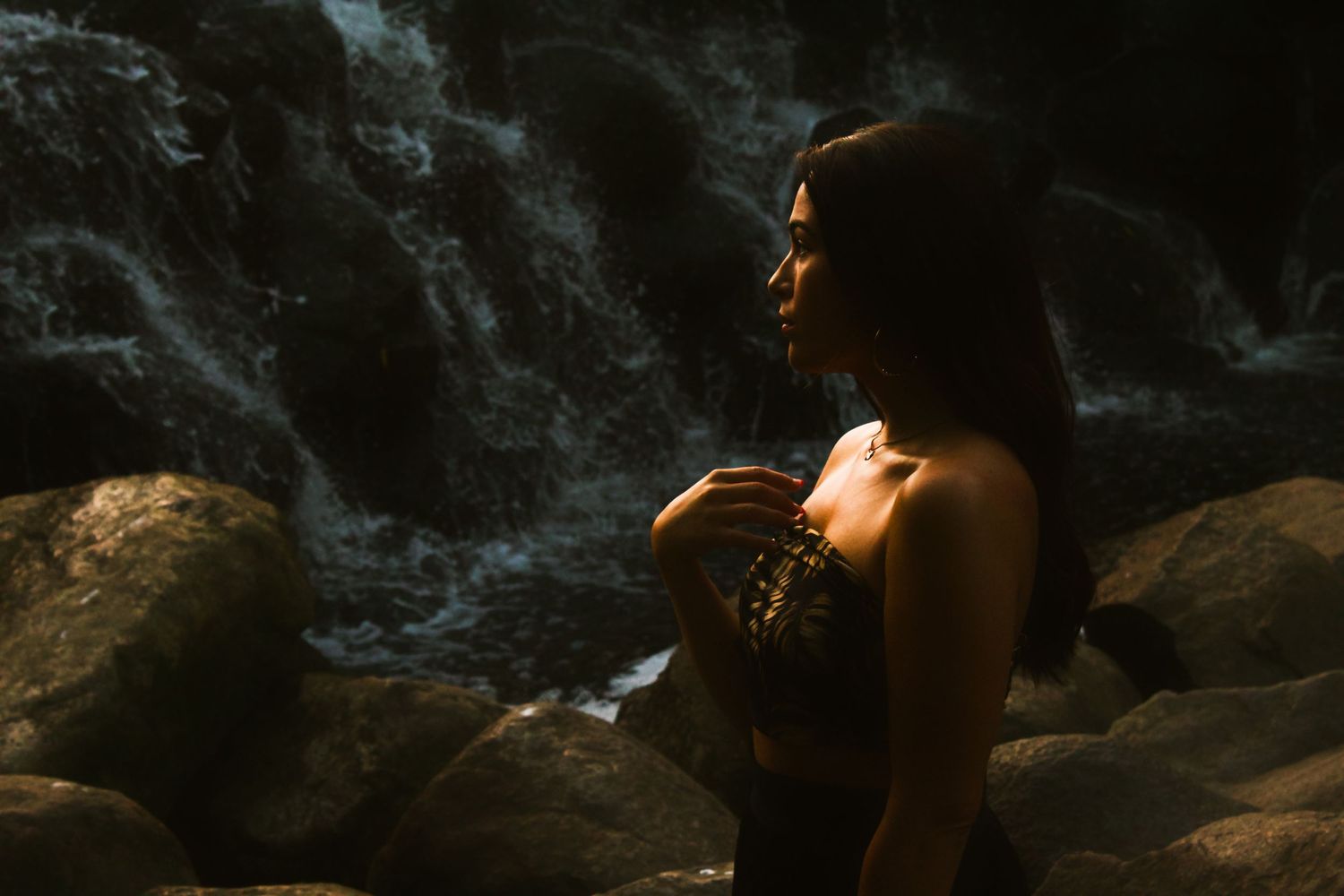 Silhouette by waterfall holding object in dramatic golden light.