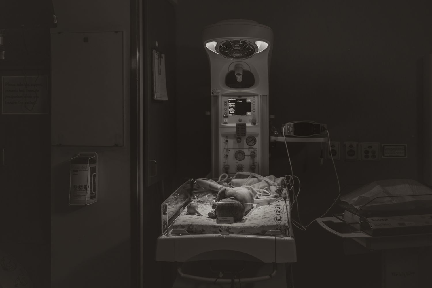 Black and white image of newborn under hospital warming light in medical setting.