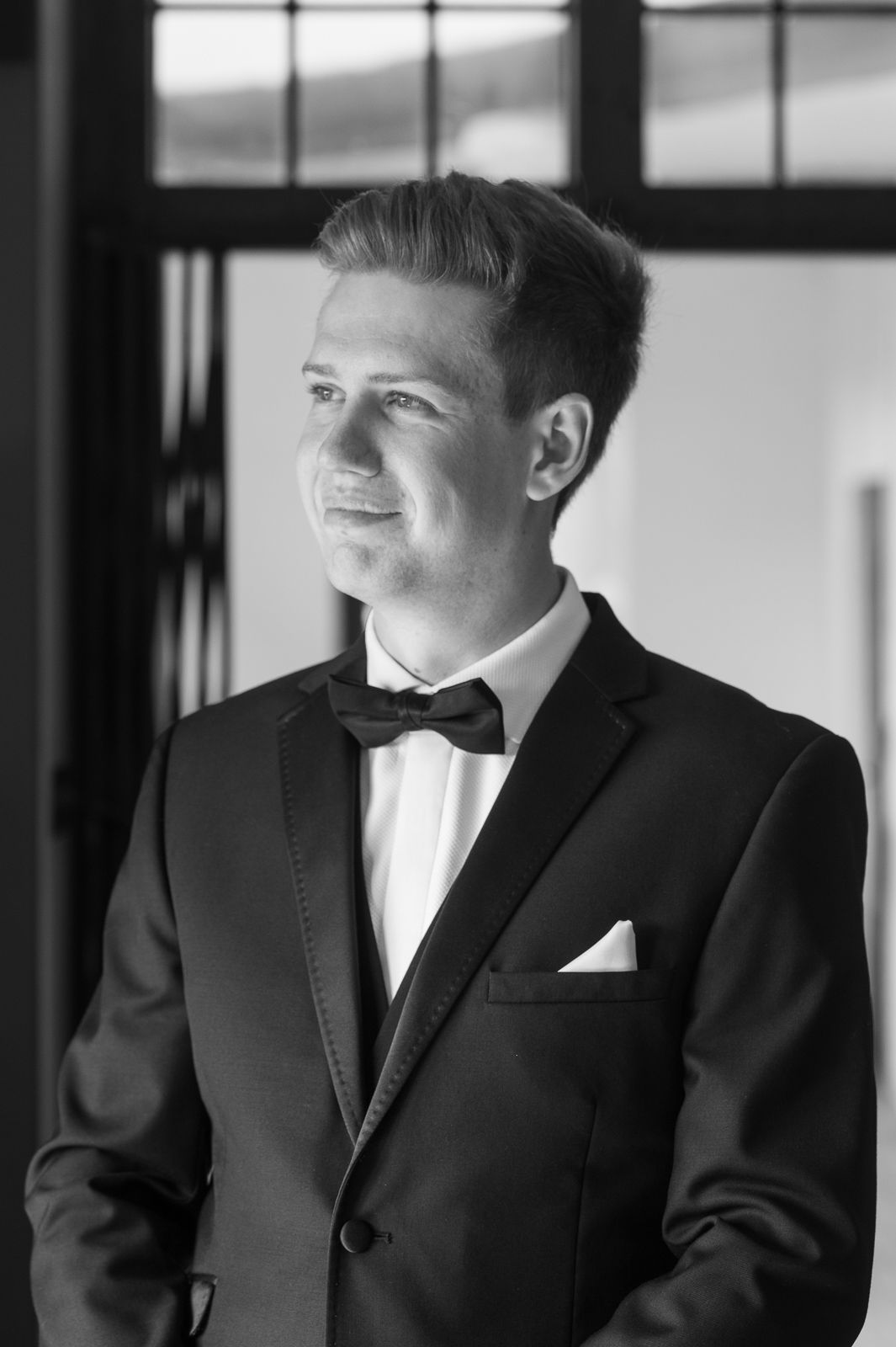Black and white portrait of a groom looking out of the window in the Mansion Room before his wedding at Port Lympne Reserve