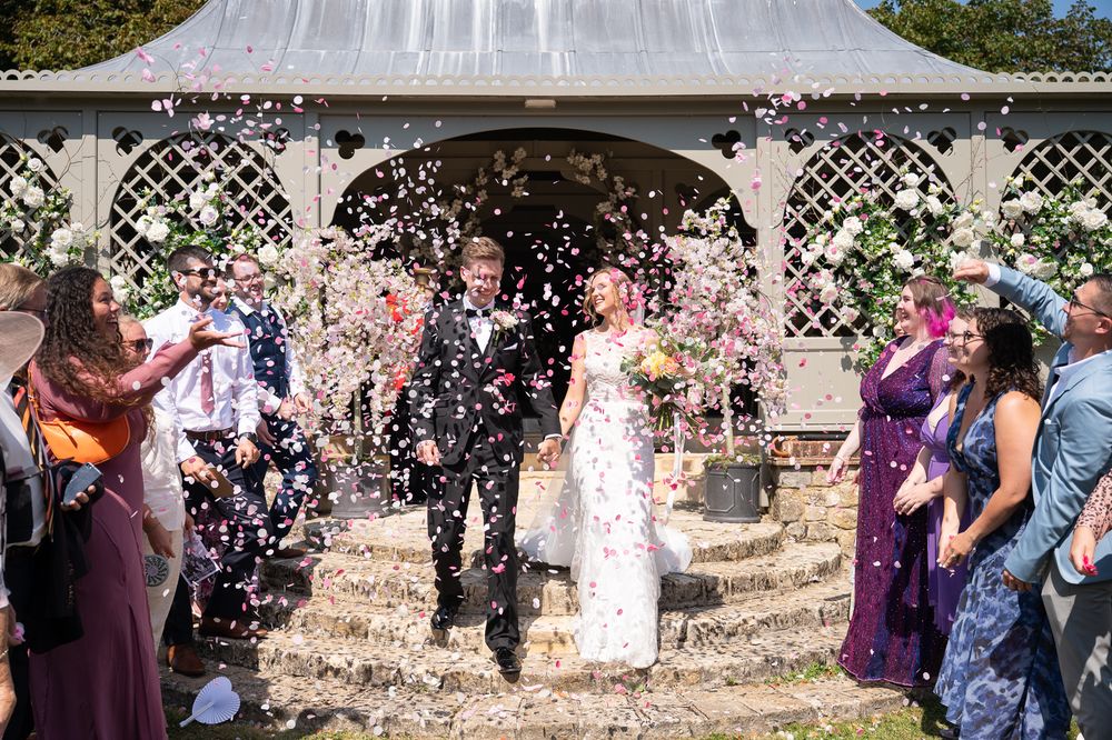 Wedding guests shower a giggling couple with confetti after their outdoor wedding ceremony at Port Lympne Reserve.