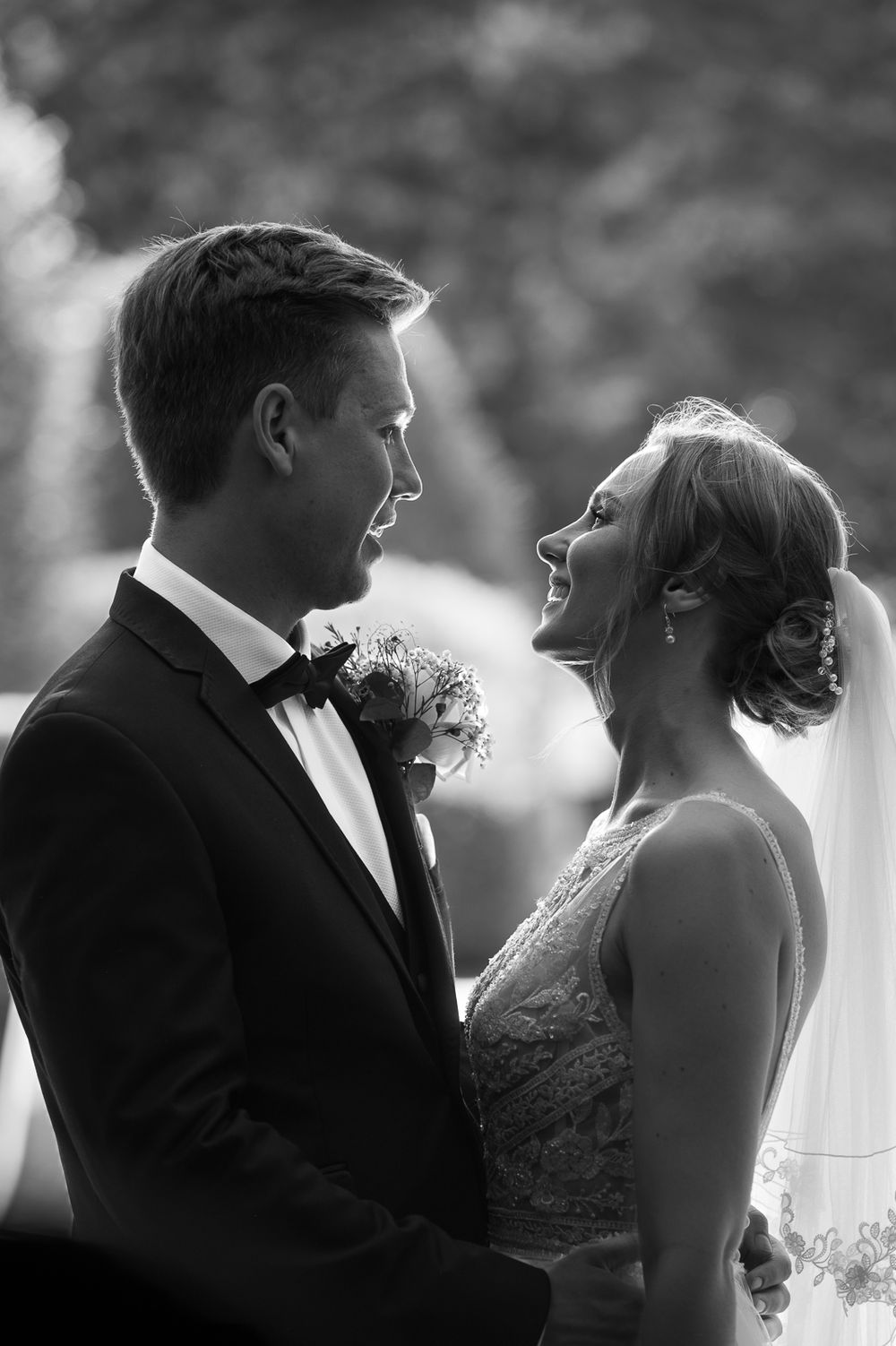 romantic black and white portrait of a bride and groom looking into each other's eyes, softly lit by gentle sun through a doorway.