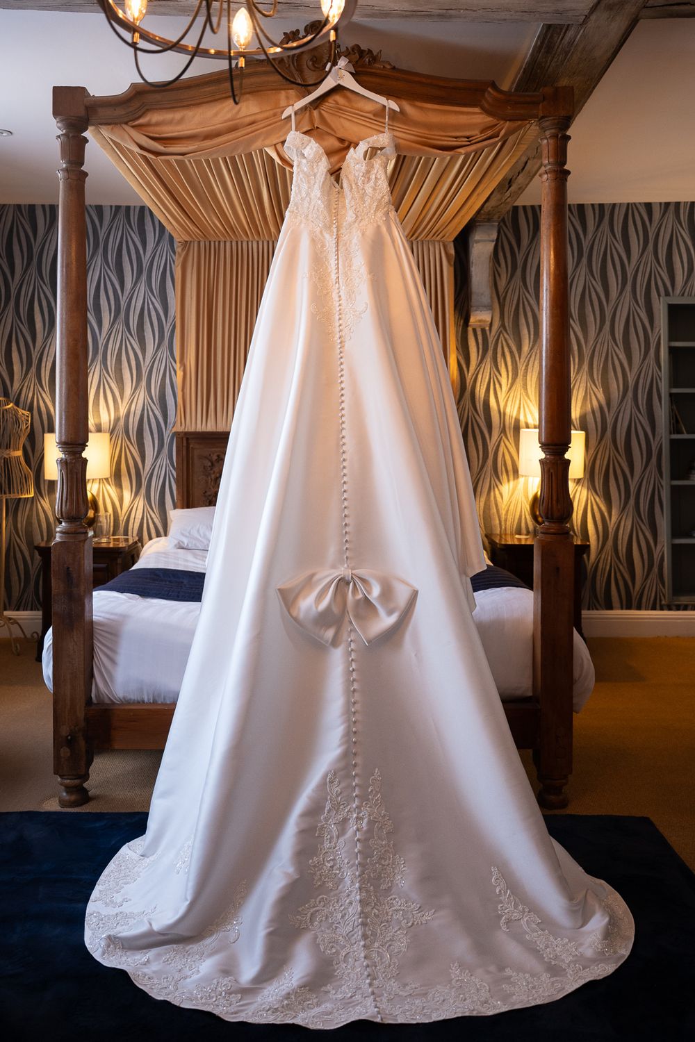 A white wedding dress with intricate beading hangs elegantly from a canopy bed in an elegantly decorated bedroom at Solton Manor.
